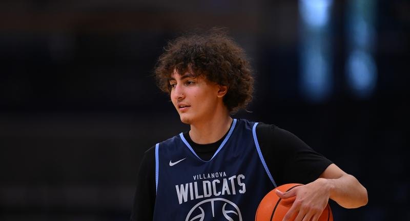 Young basketball player in a Villanova Wildcats jersey dribbling a ball on an indoor court.