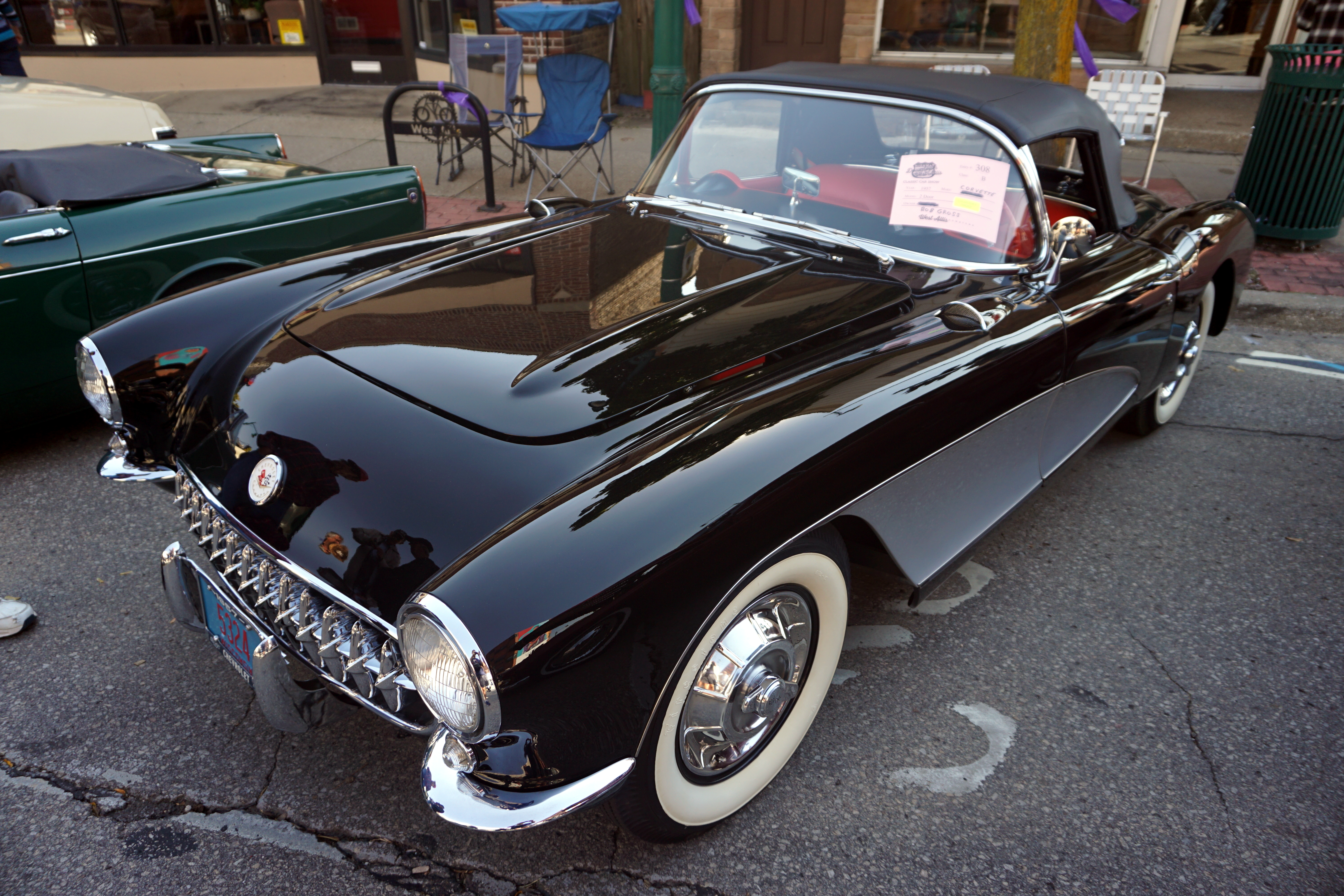 Black 1957 Chevrolet Corvette convertible with whitewall tires at an outdoor car show.