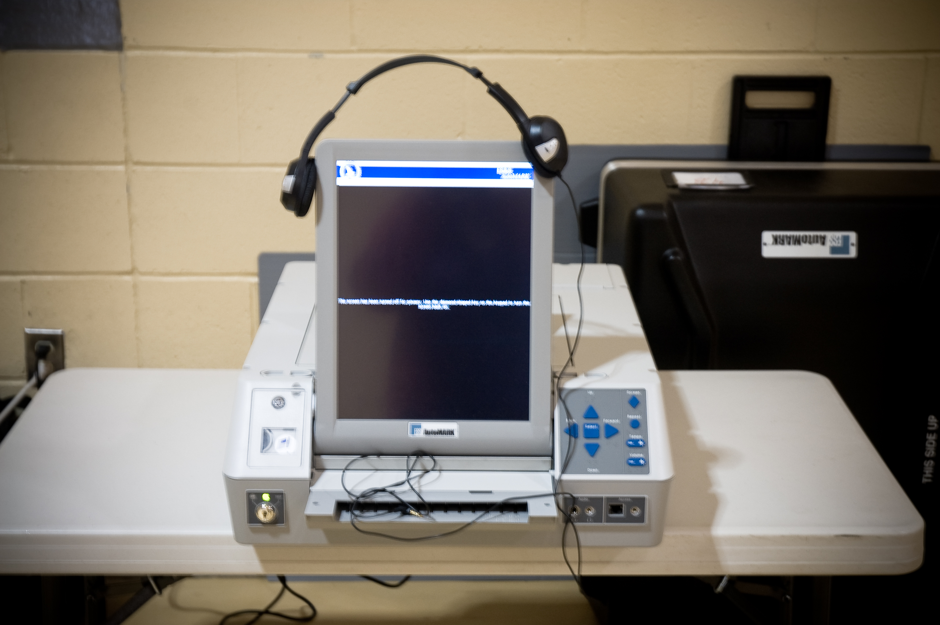 An electronic voting device with a monitor and headphones on a table.
