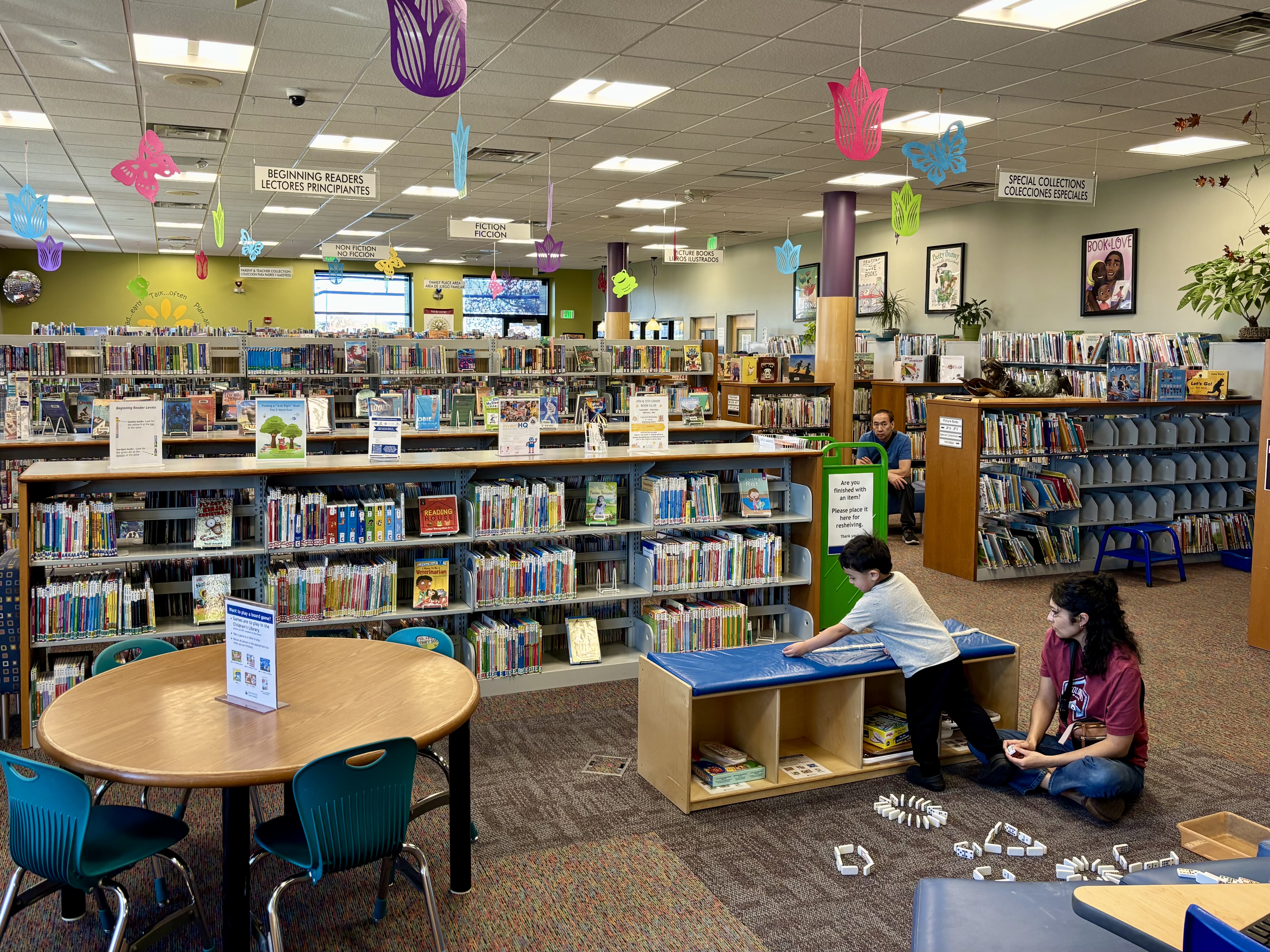 Colorful children's library interior with bookshelves, hanging decorations, and a small round table.