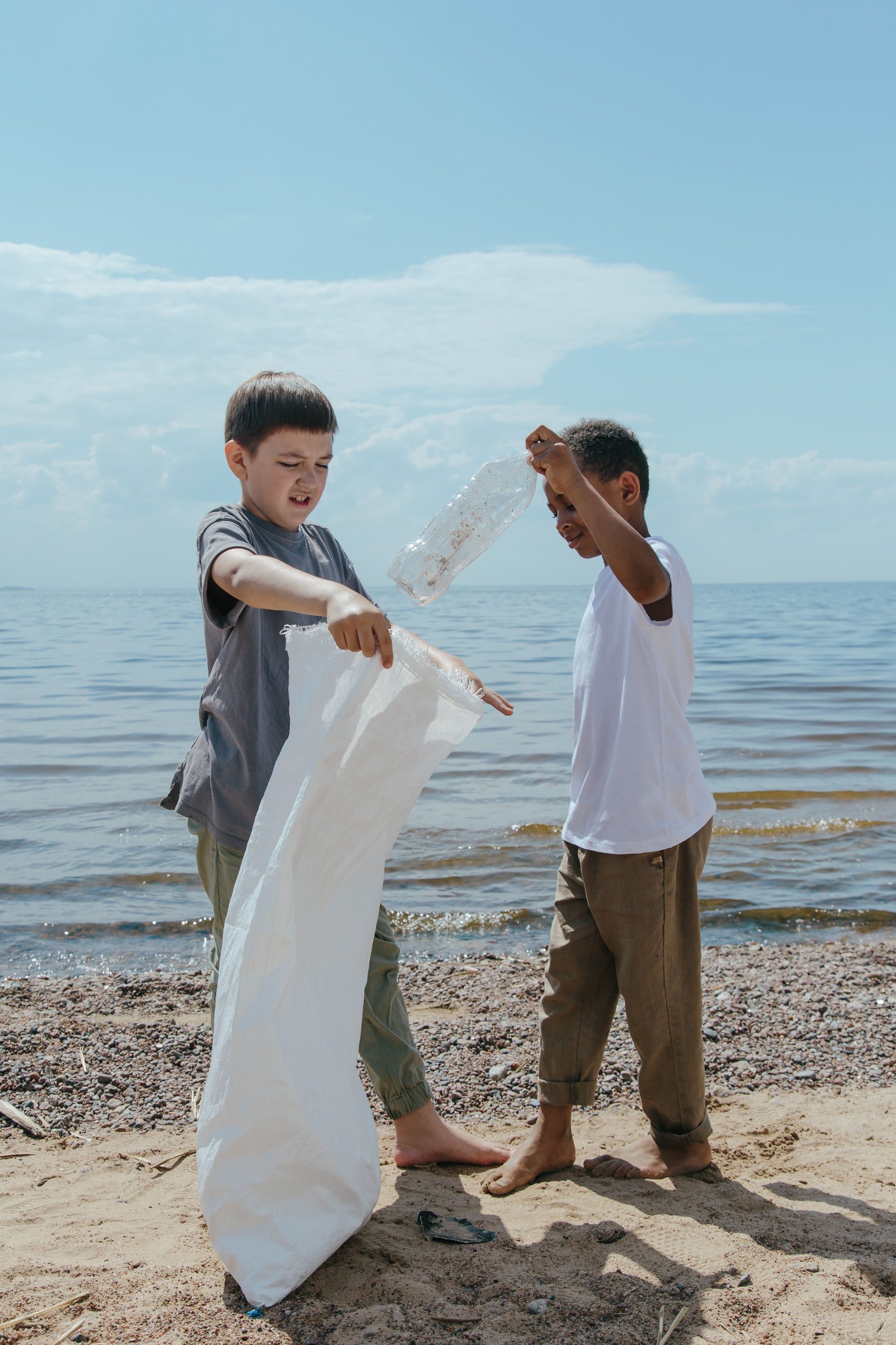 Two boys clean a beach, picking up litter to promote environmental sustainability.