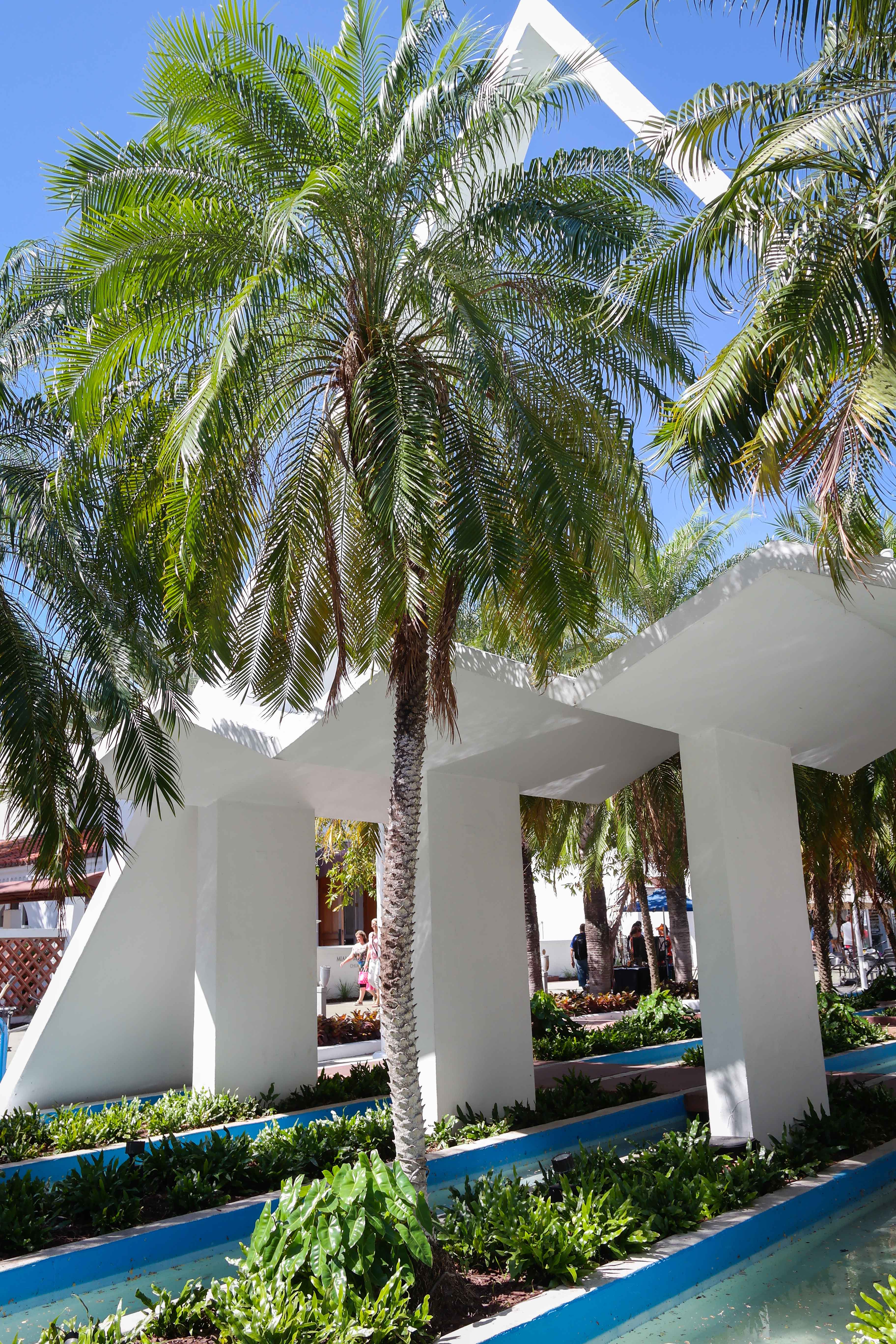 Tall white angular modernist columns and arched canopy framed by palm trees.
