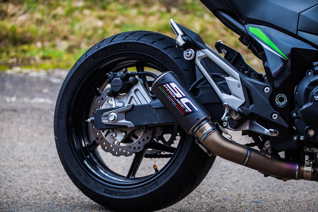 Close-up of a motorcycle's rear wheel, disc brake, and aftermarket exhaust pipe.