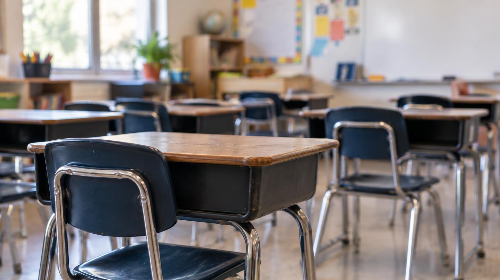 Rows of empty student desks in a sunlit classroom.