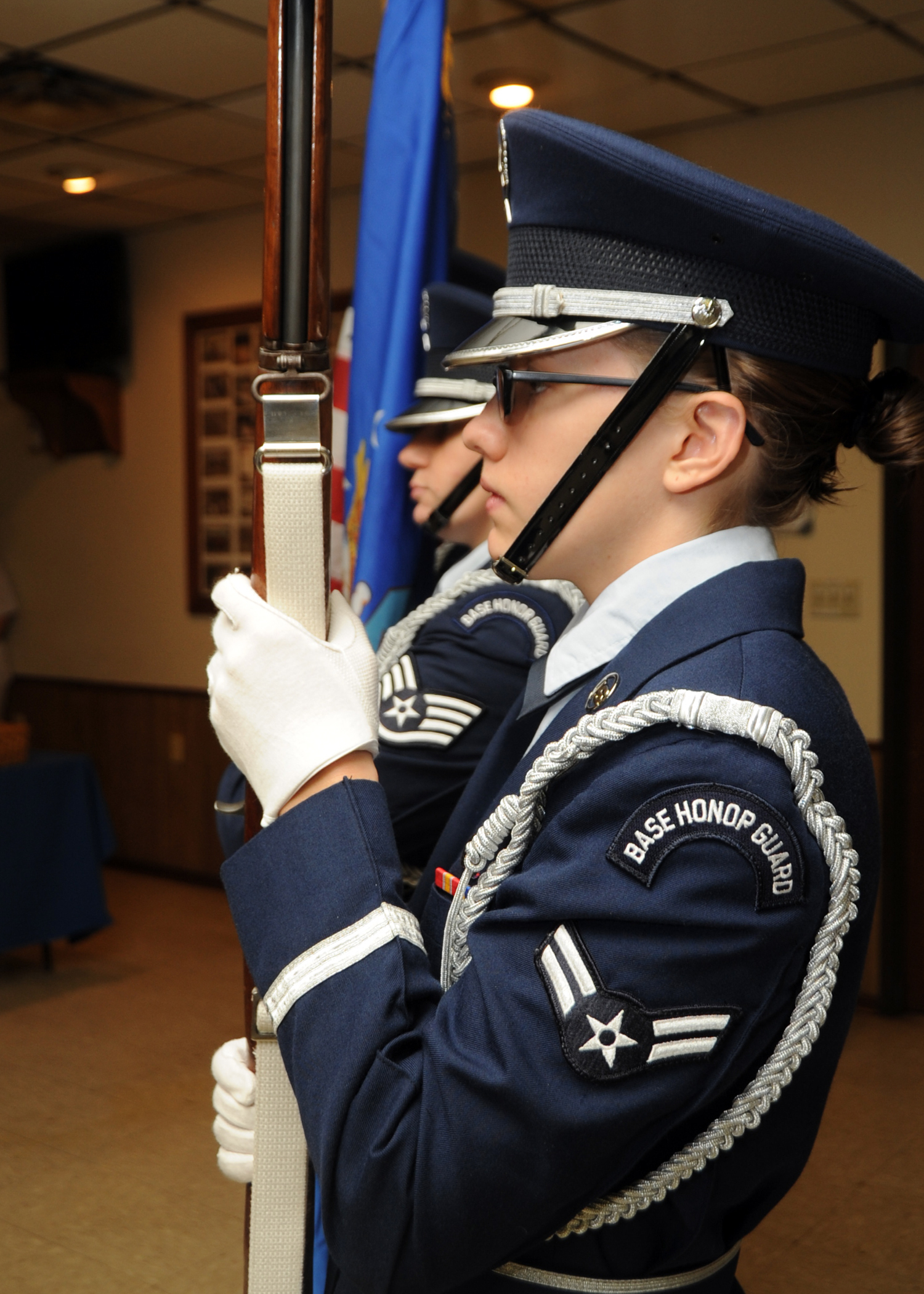 Air Force honor guard members in dress blue uniforms stand at attention indoors.