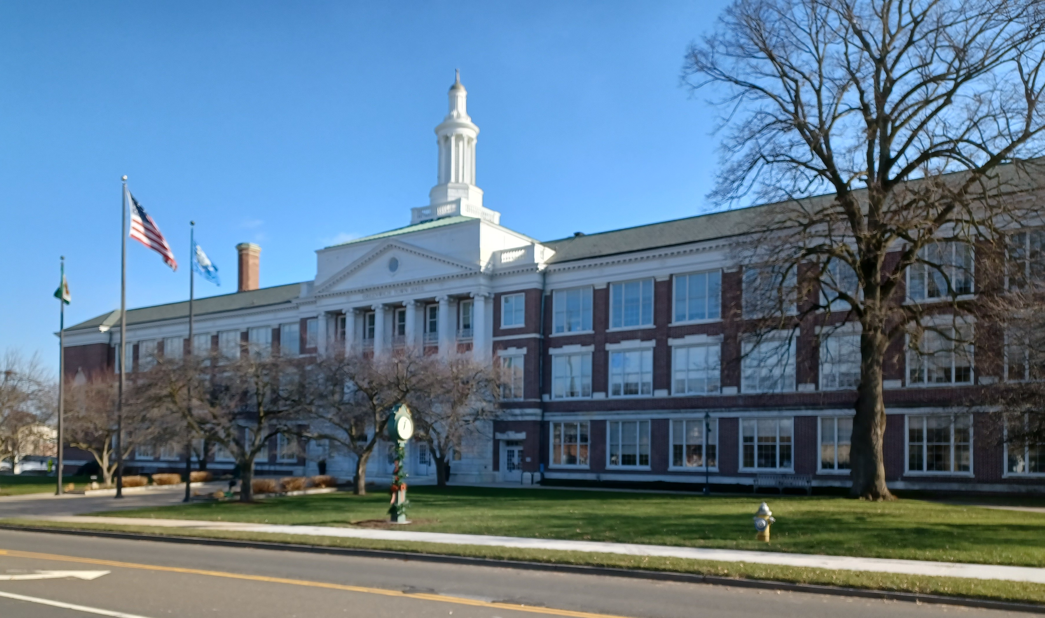 Exterior of Greenwich Town Hall, a brick and white colonial building with a cupola and flagpole on a clear day.