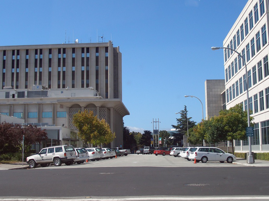 Two large government office buildings flanking a parking lot on a clear day.