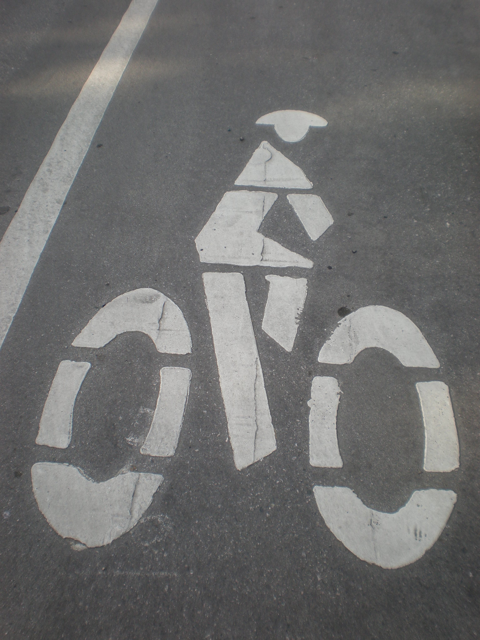 White bicycle lane symbol painted on worn asphalt road surface.