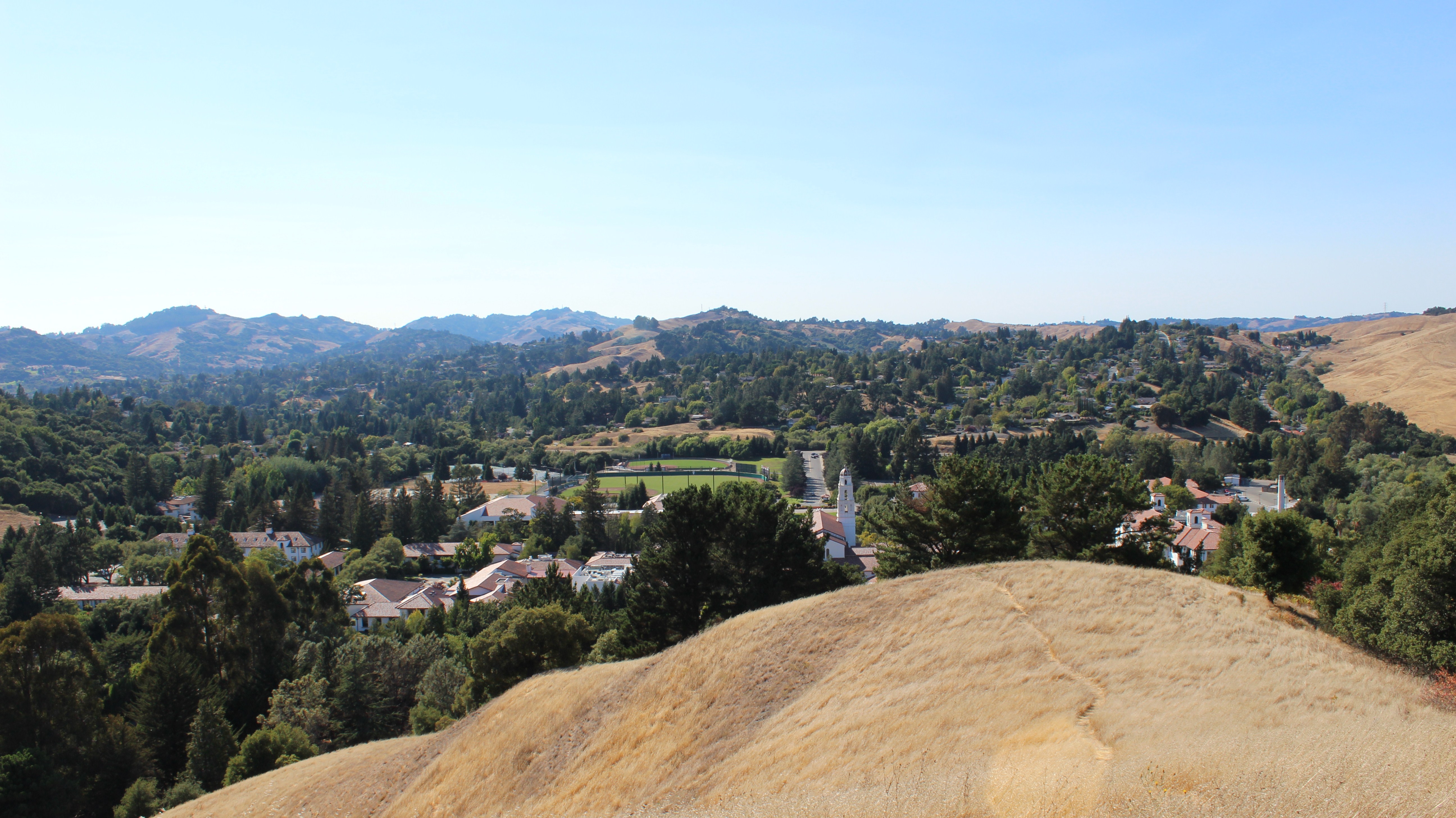 Aerial view of a college campus nestled in a valley surrounded by golden hills and green trees.