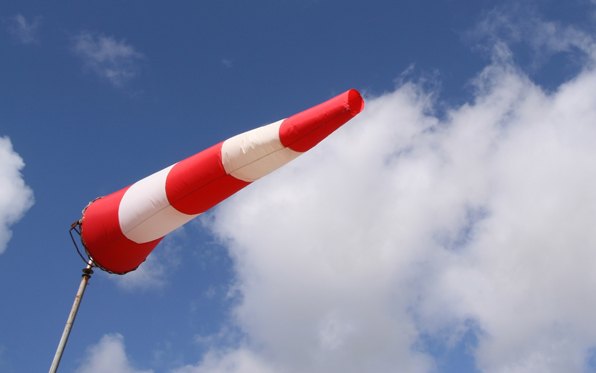 Red-and-white striped windsock blown fully horizontal by strong wind against a blue sky.