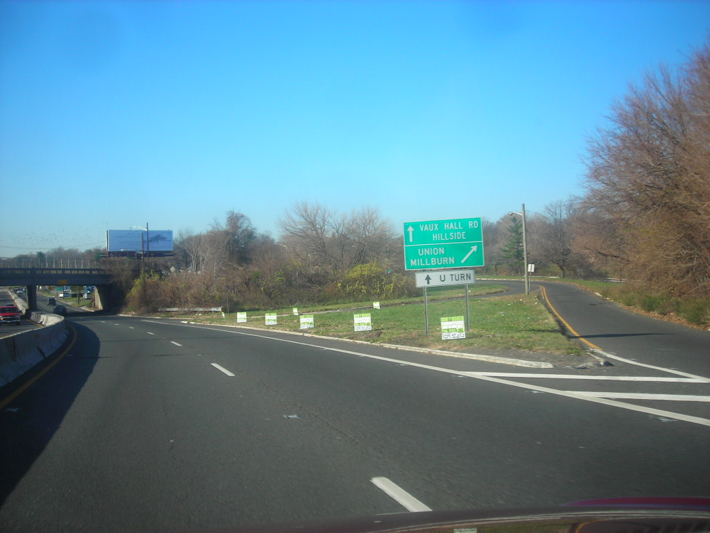 Multi-lane highway with green exit signs for Vaux Hall Road, Union, and Millburn, and a U-turn sign.
