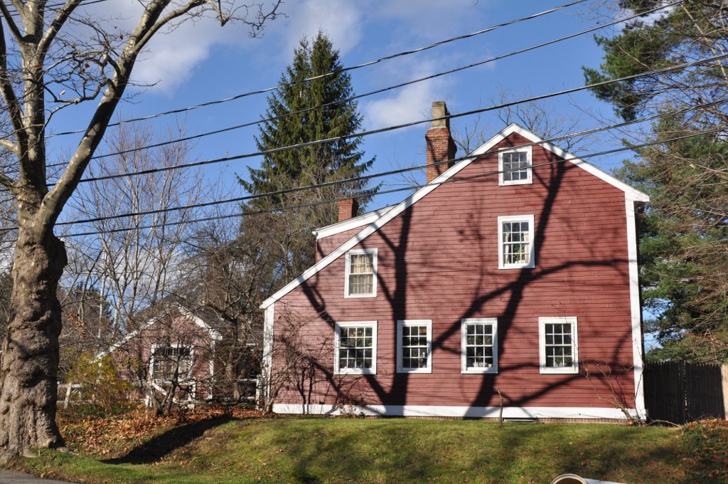 A large red colonial-style house with white-trimmed windows on a residential street.