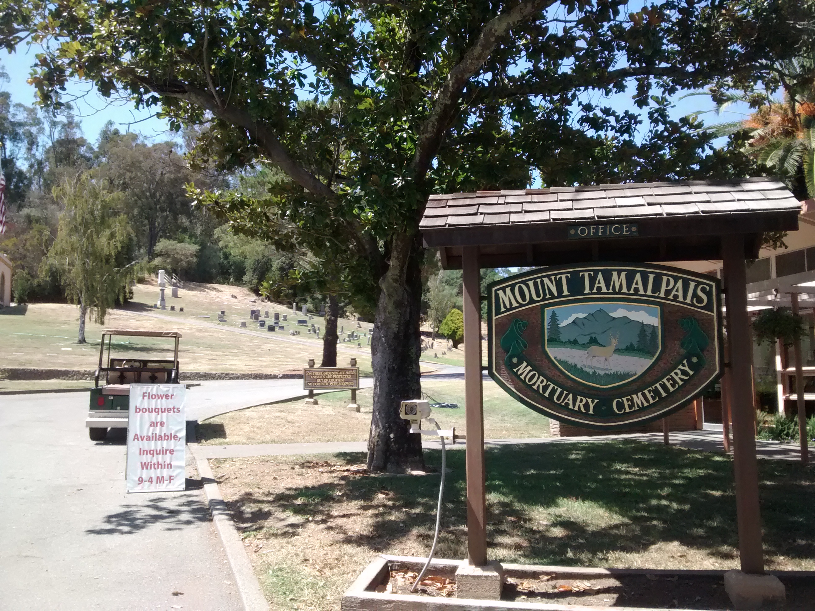 Entrance sign for a mortuary and cemetery with a tree-lined hillside in the background.