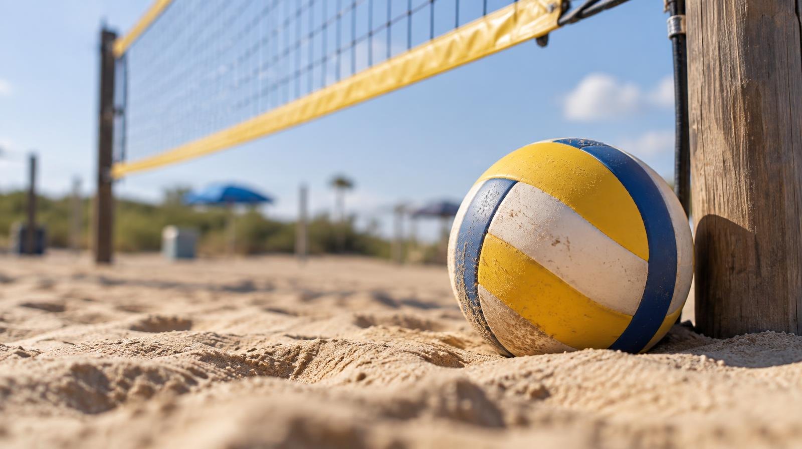A beach volleyball resting on sand beside a net post on an outdoor court.