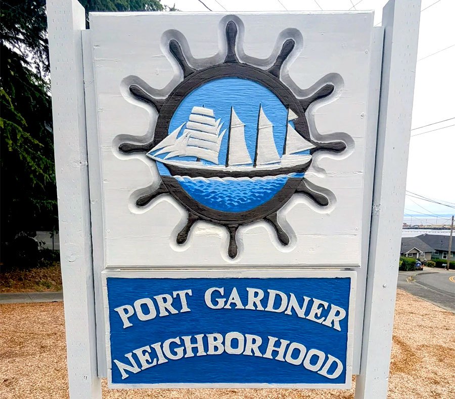 White wooden neighborhood entrance sign reading 'Port Gardner Neighborhood' with a ship's wheel emblem.