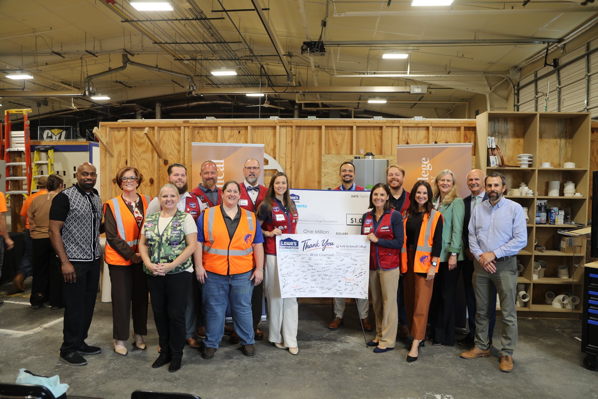 Group of people in business attire and orange safety vests holding a large ceremonial check for one million dollars.
