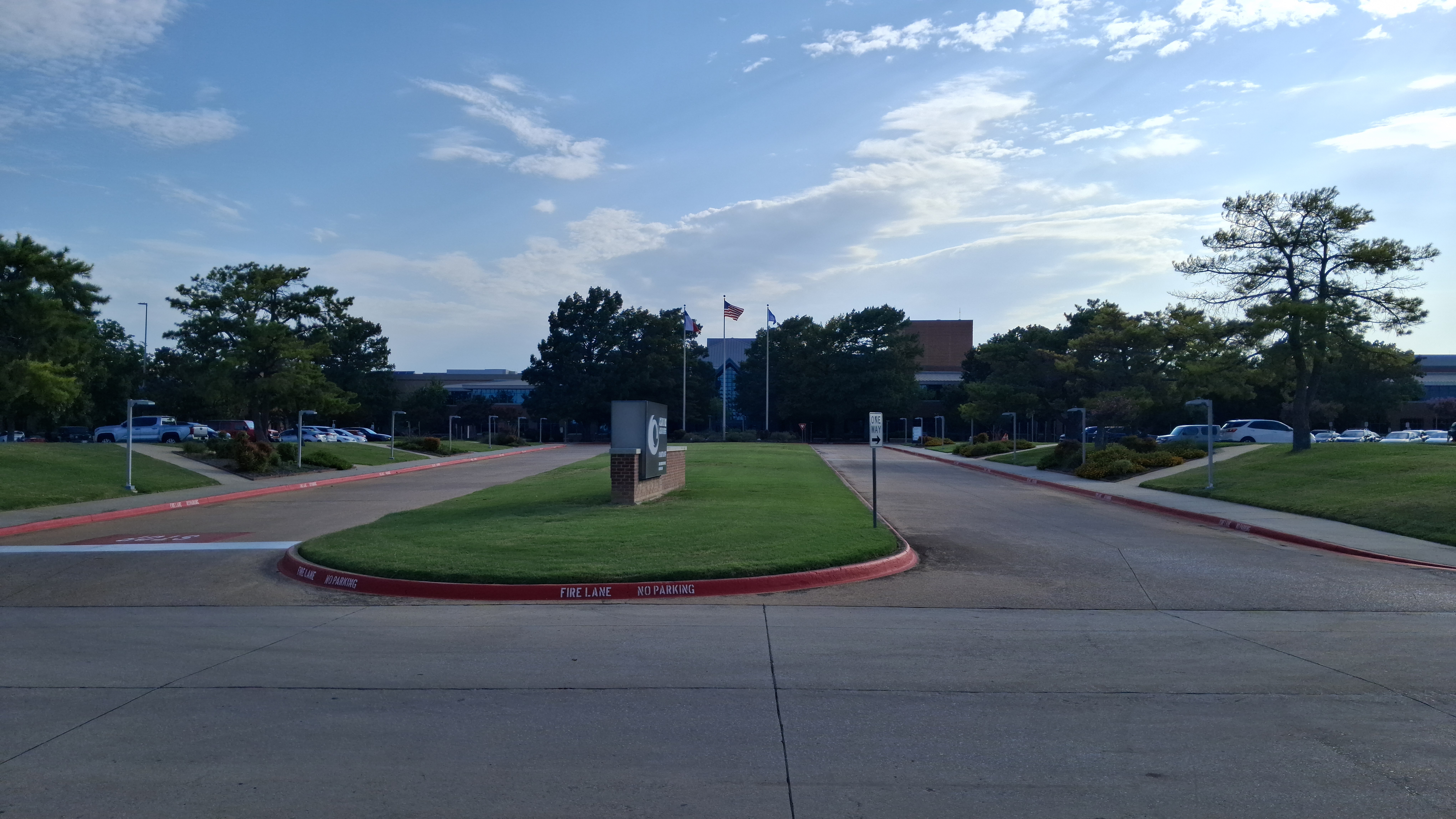 Campus entrance with a circular median, monument sign, flagpoles, and a brick building.