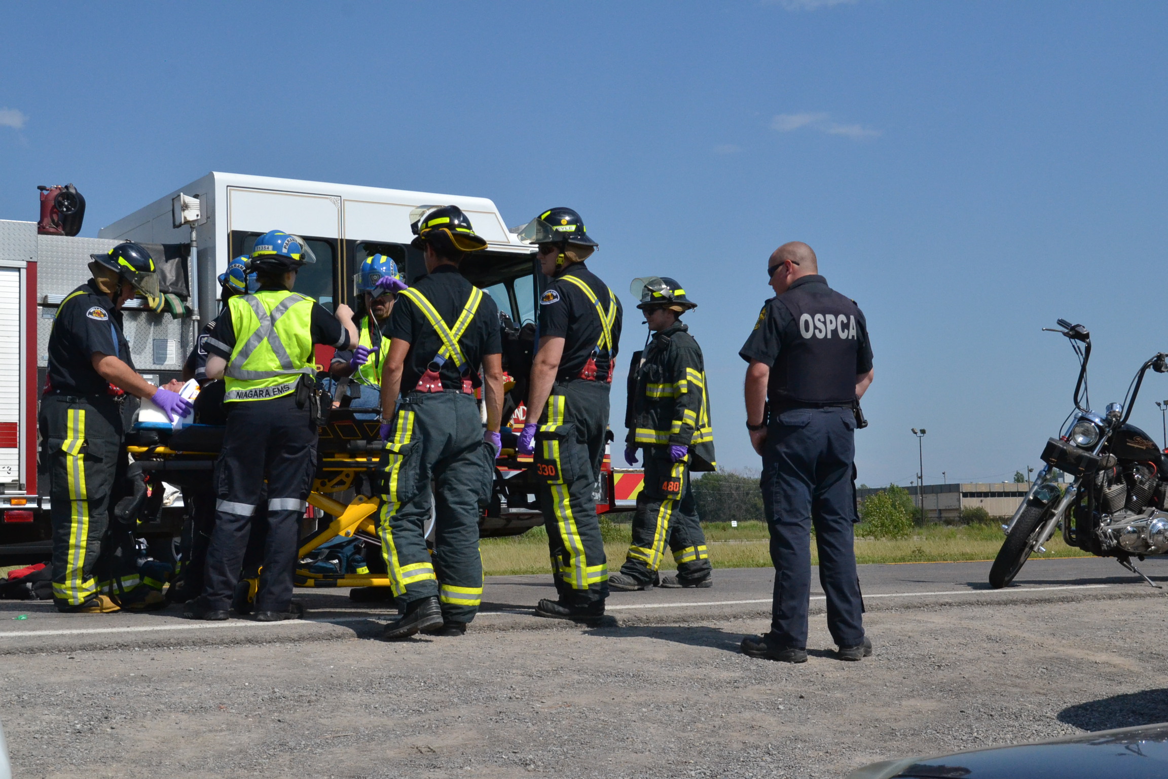 Firefighters and paramedics load a gurney into an ambulance at a motorcycle crash scene.