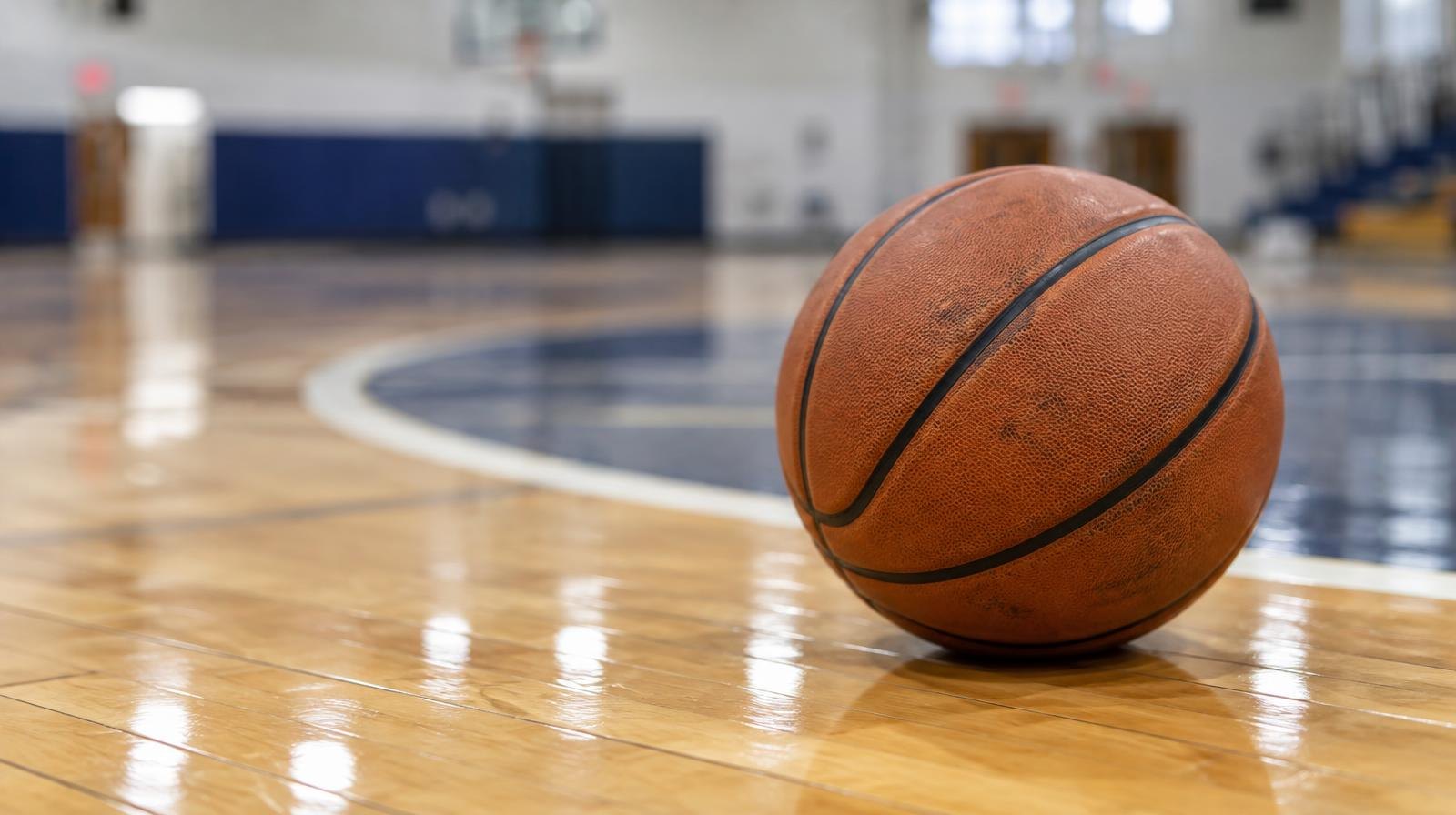 A basketball resting on a hardwood gymnasium floor near the center court circle.