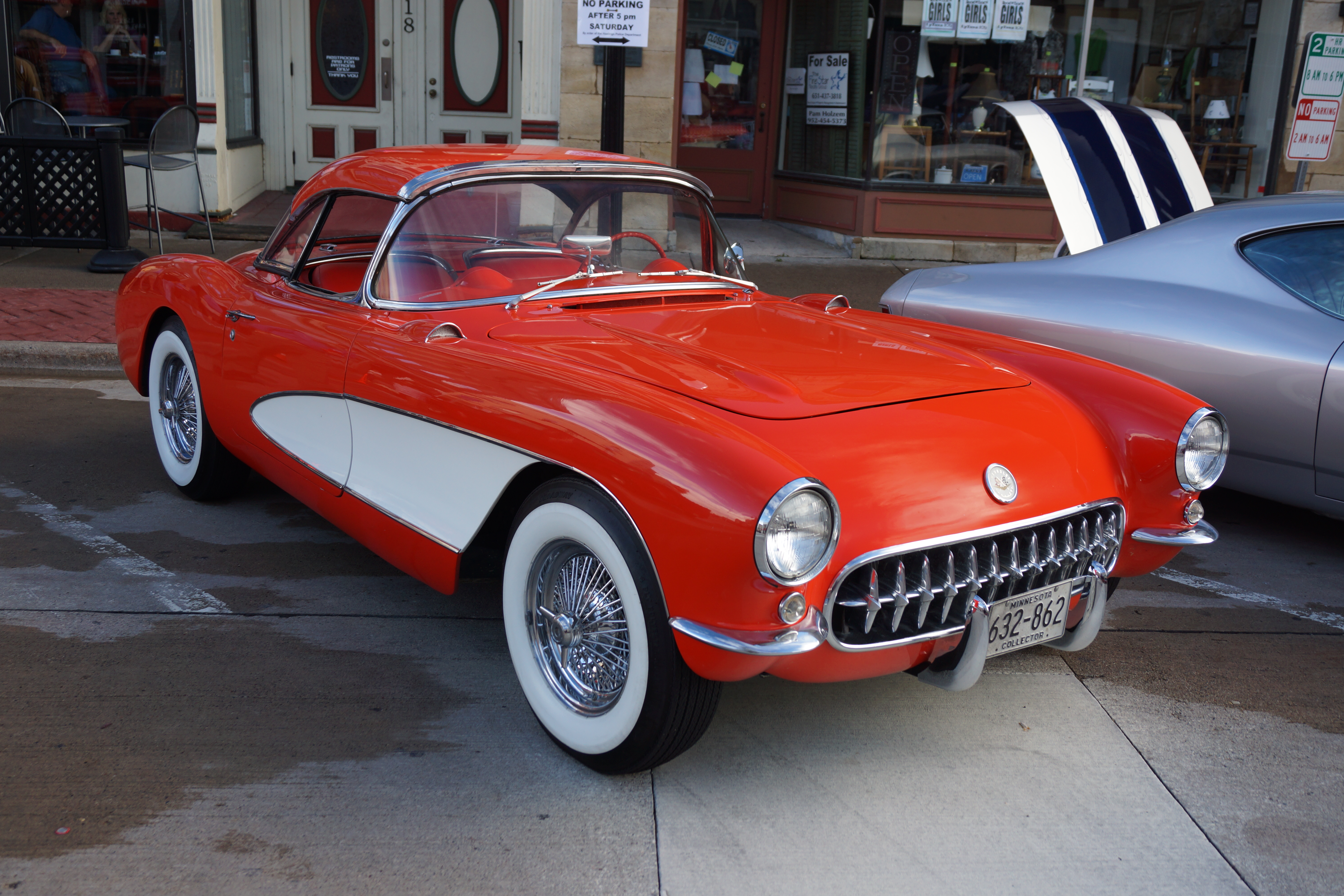 Red and white 1956 Chevrolet Corvette with whitewall tires parked at a car show.