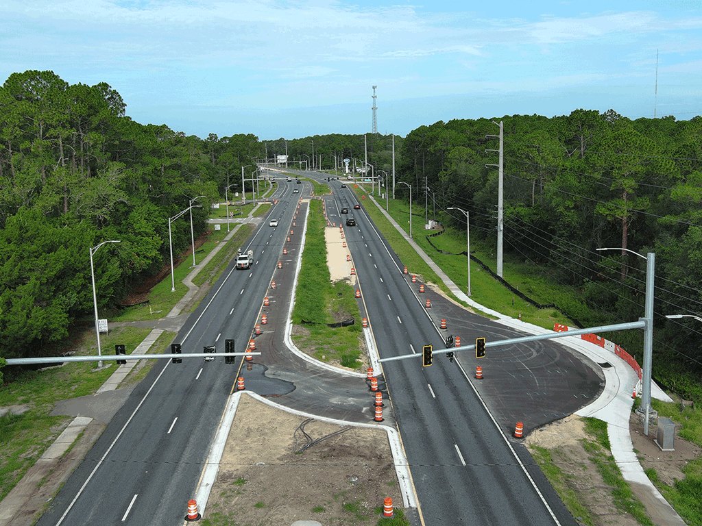 Aerial view of a divided multi-lane highway with orange construction barrels and traffic signals.