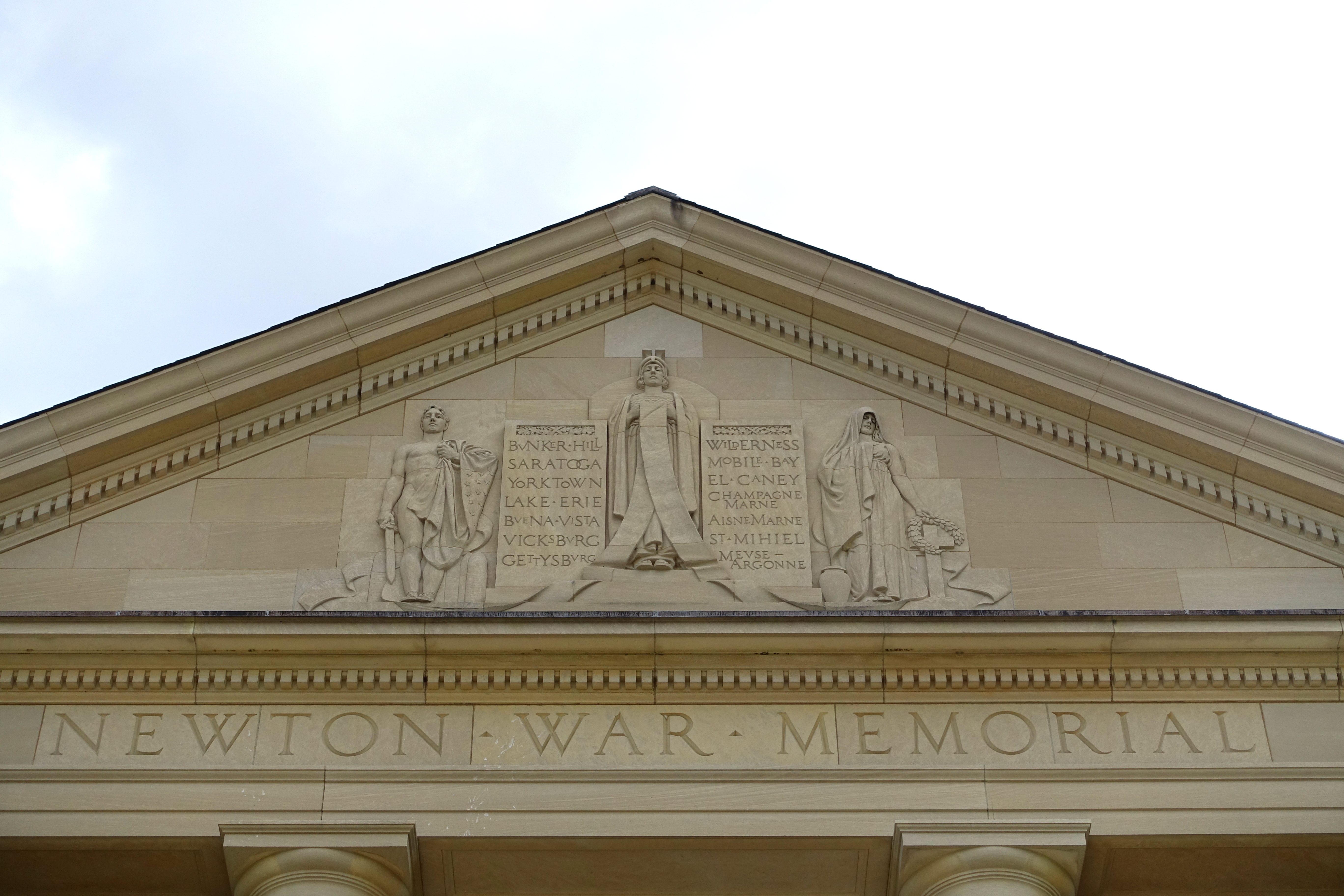 Neoclassical stone pediment with carved relief figures and inscribed text on a civic building.
