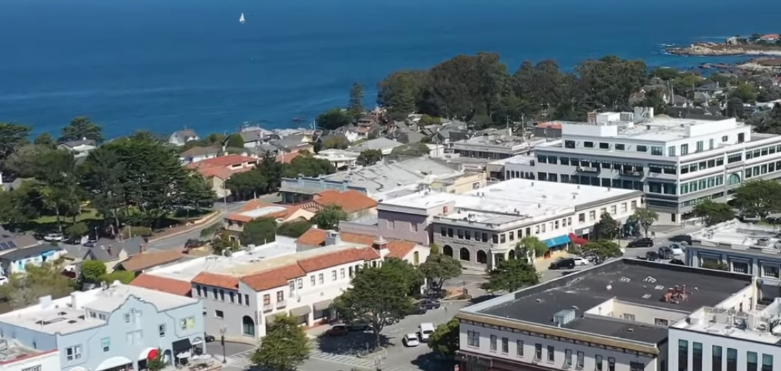 Aerial view of a small coastal downtown with red-roofed buildings and a bay beyond.