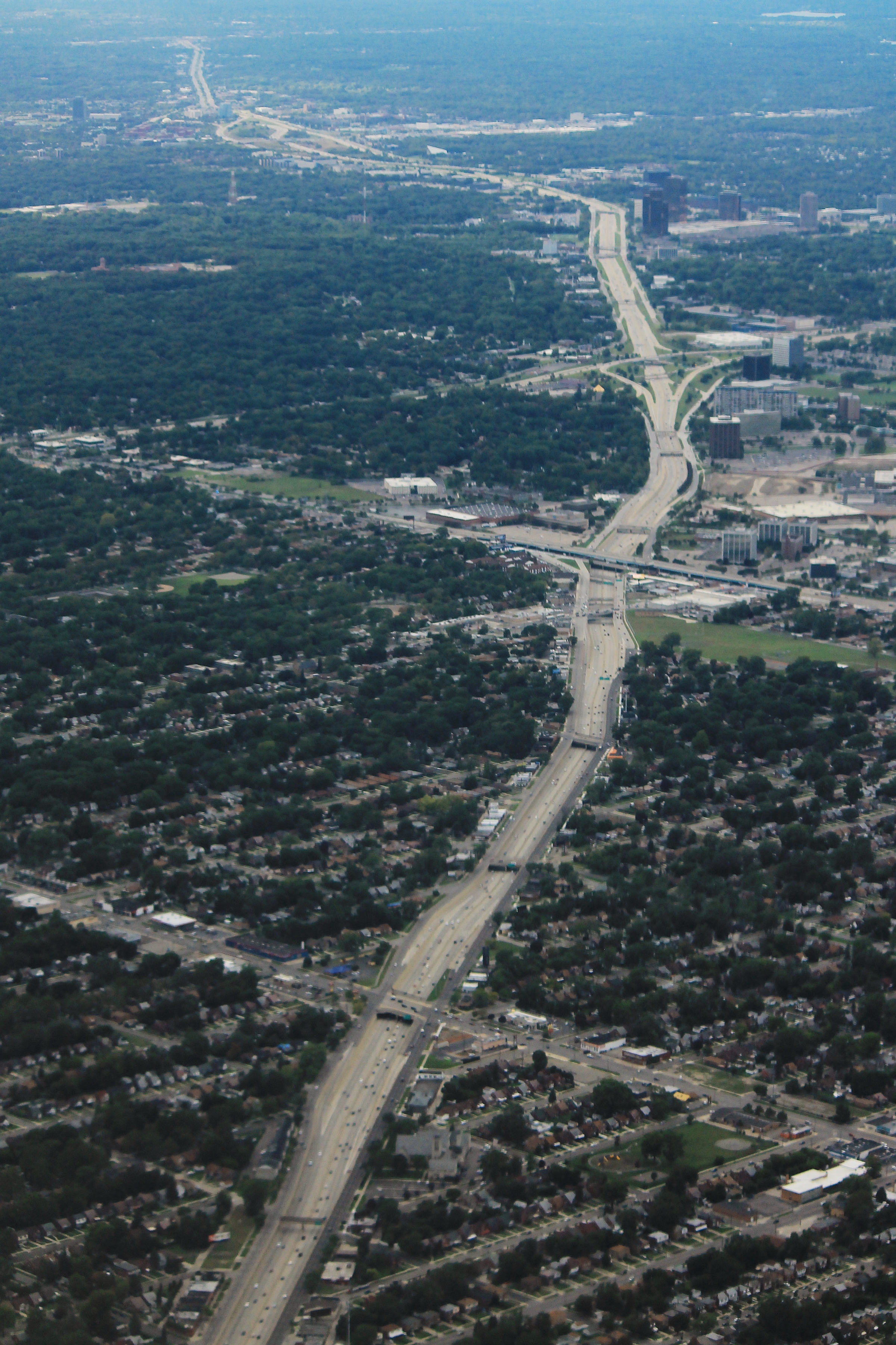 Aerial view of a multi-lane freeway cutting through a densely wooded urban neighborhood.