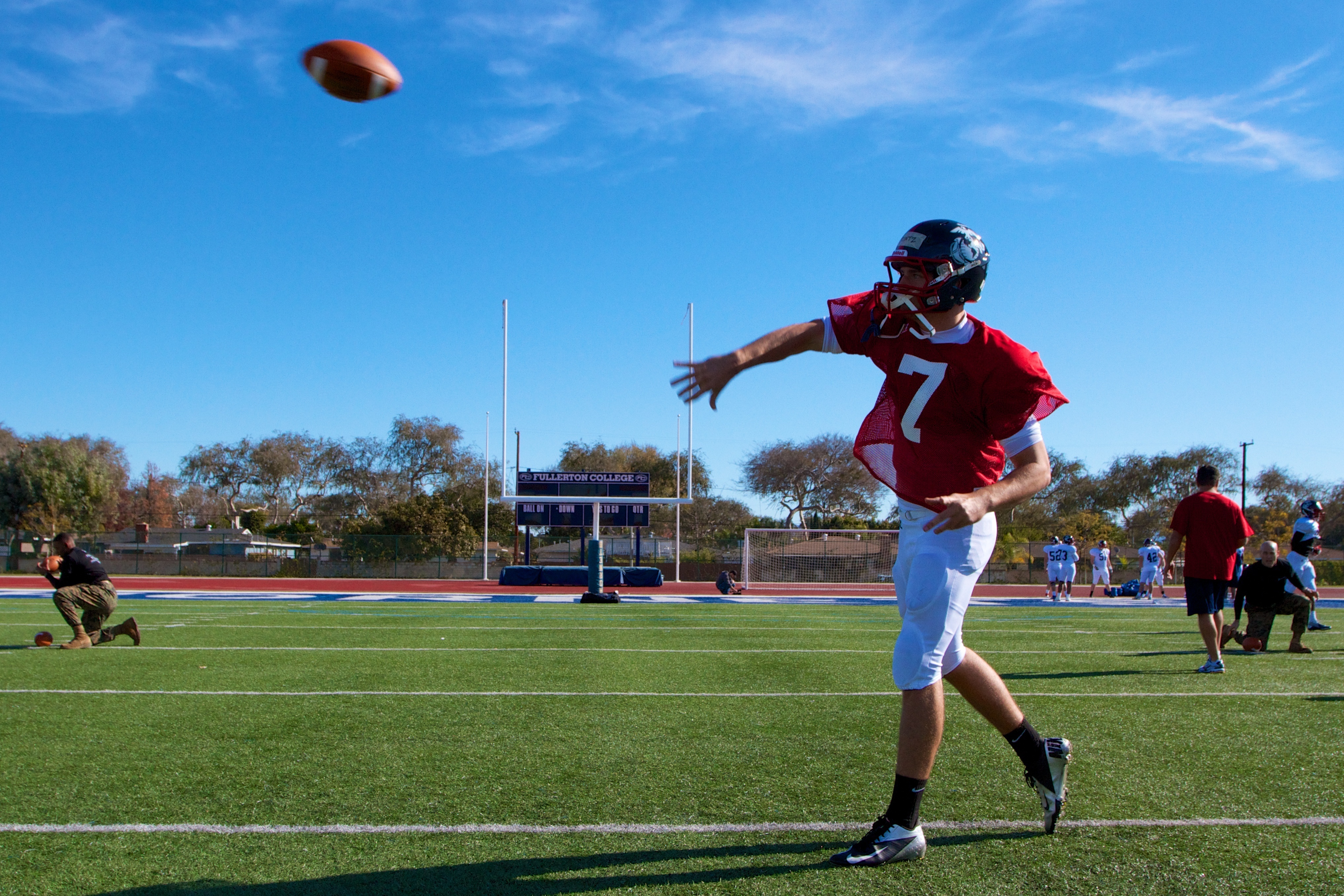 A quarterback in a red jersey throws a football on a turf field.