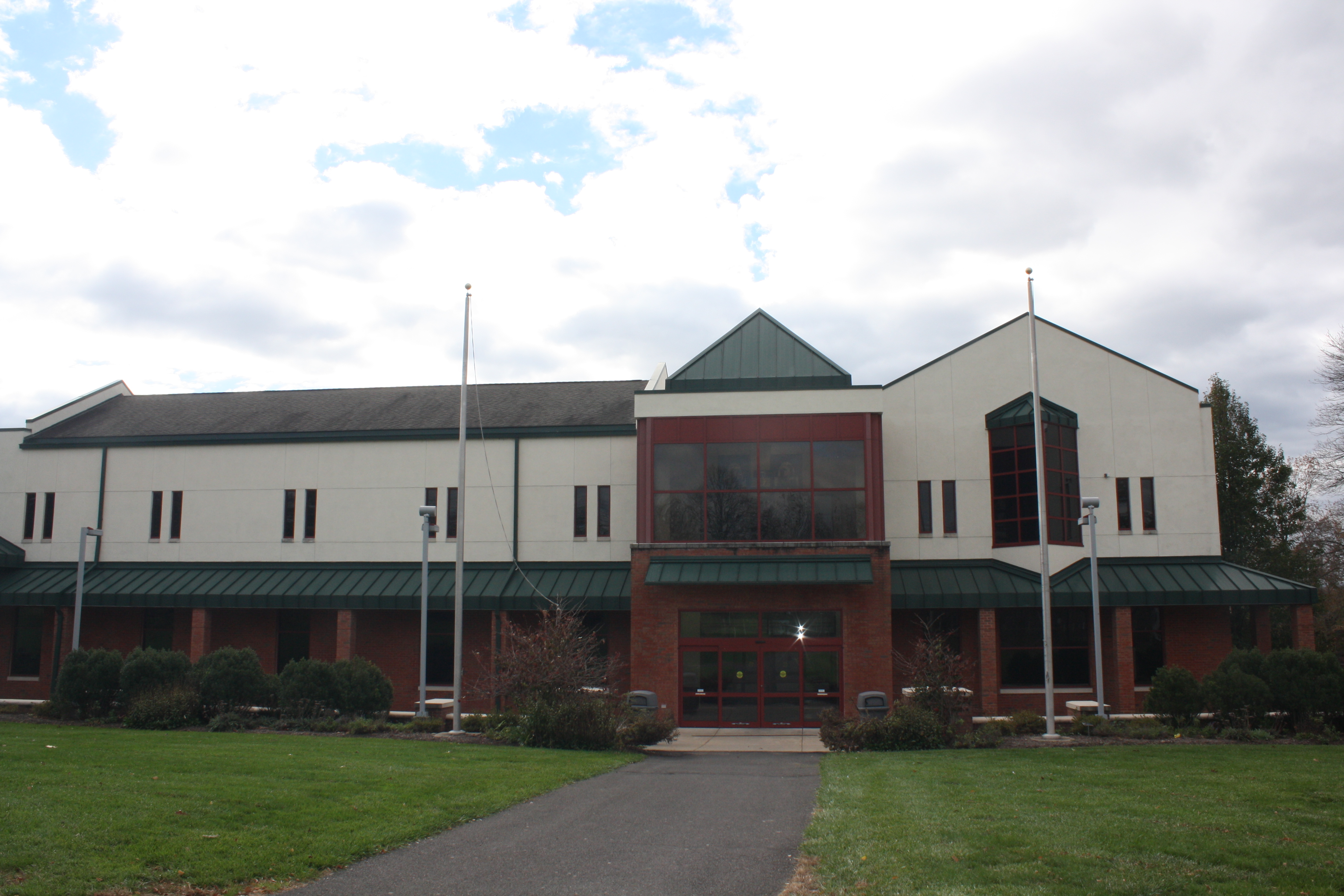 Two-story institutional building with green metal roof and flagpoles on a college campus.