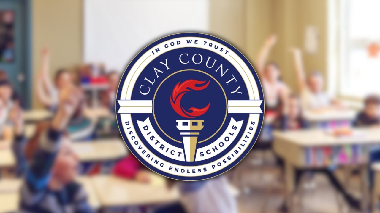 Clay County District Schools circular seal with torch emblem and blurred classroom in background.