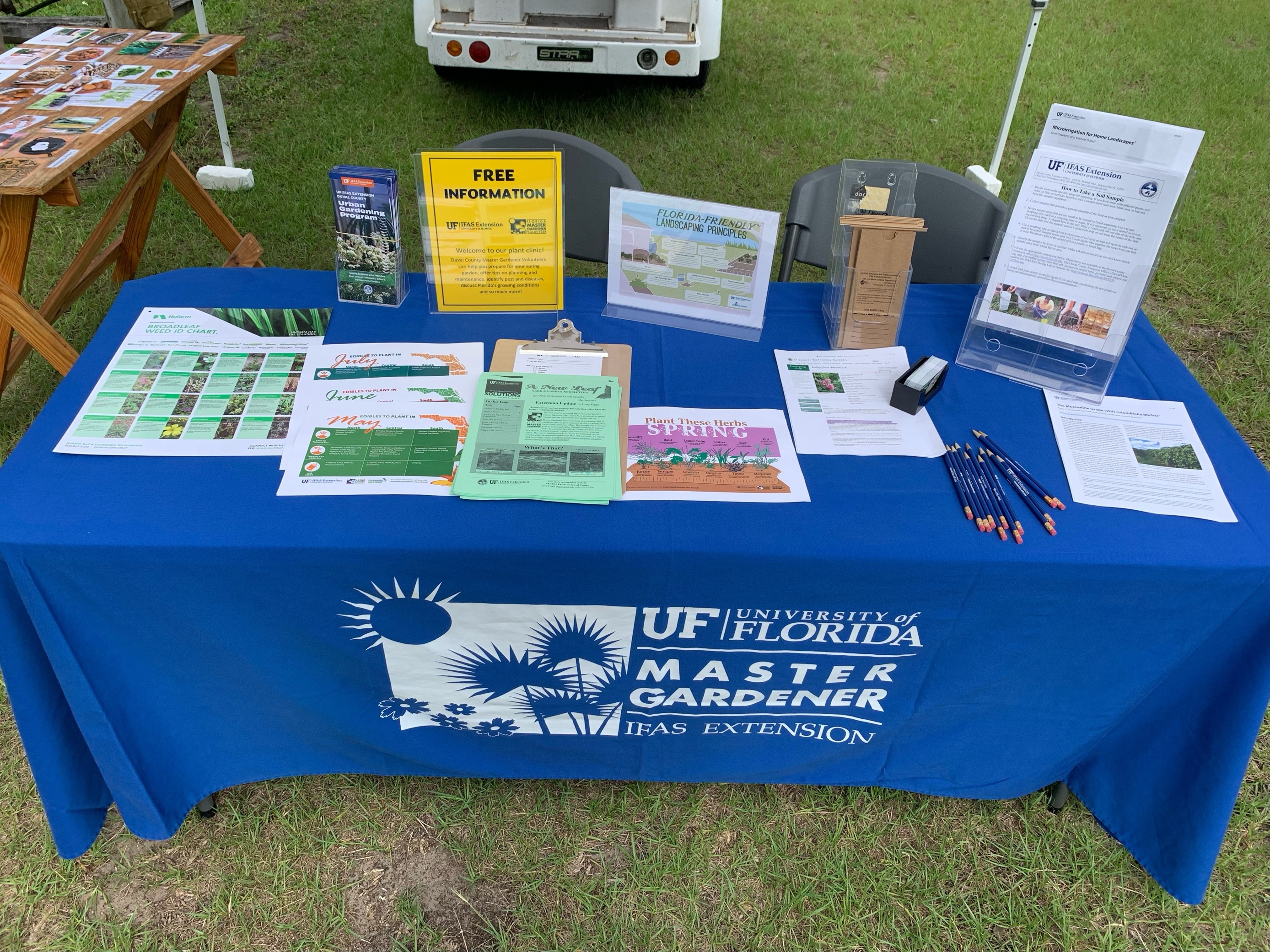 Outdoor table with blue UF/IFAS Master Gardener tablecloth, brochures, and a wooden insect house.