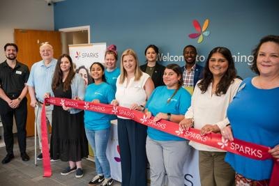 Group of people holding a red SPARKS-branded ribbon at a ribbon-cutting ceremony inside a learning center.