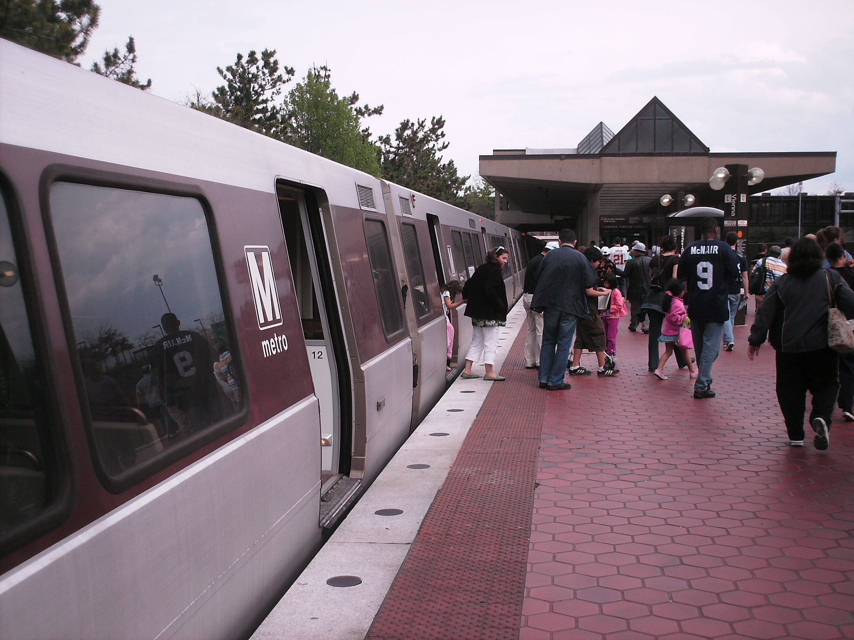 Passengers walking along a brick platform at a Metro station with a distinctive angular roof shelter.