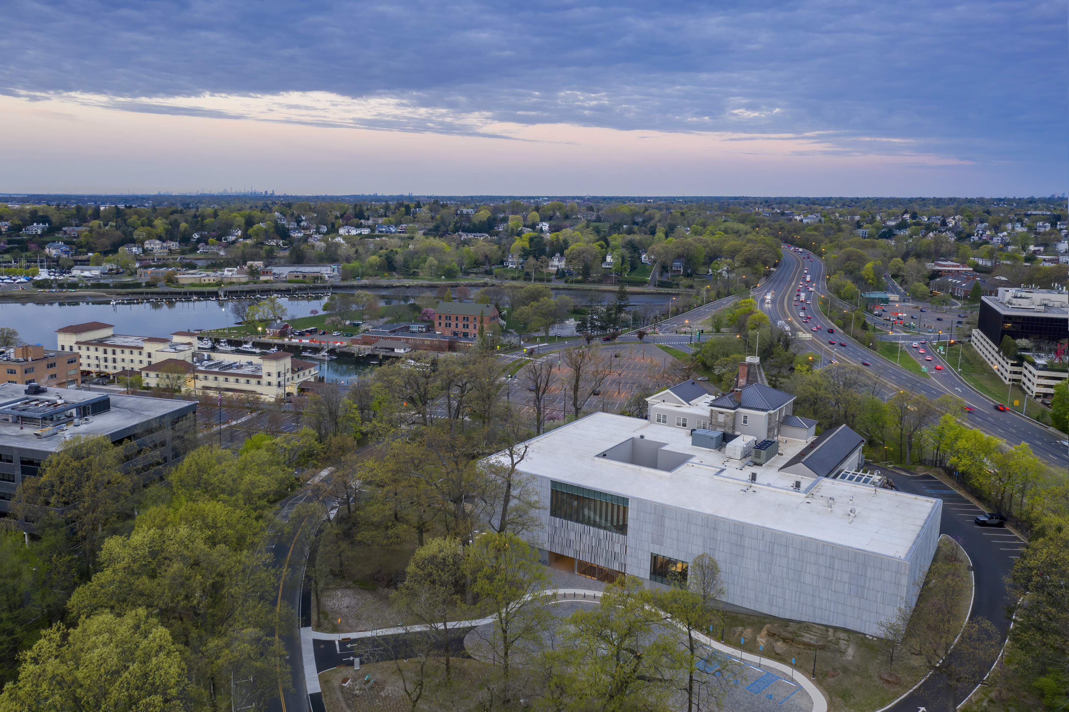 Aerial view of a modern museum building surrounded by trees near a road and water.