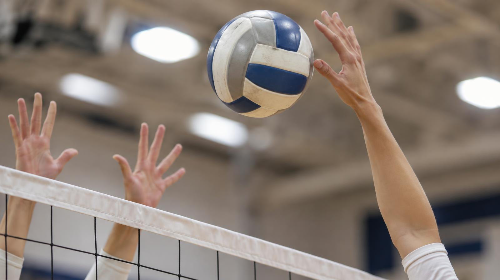 Close-up of a volleyball being spiked over a net indoors.