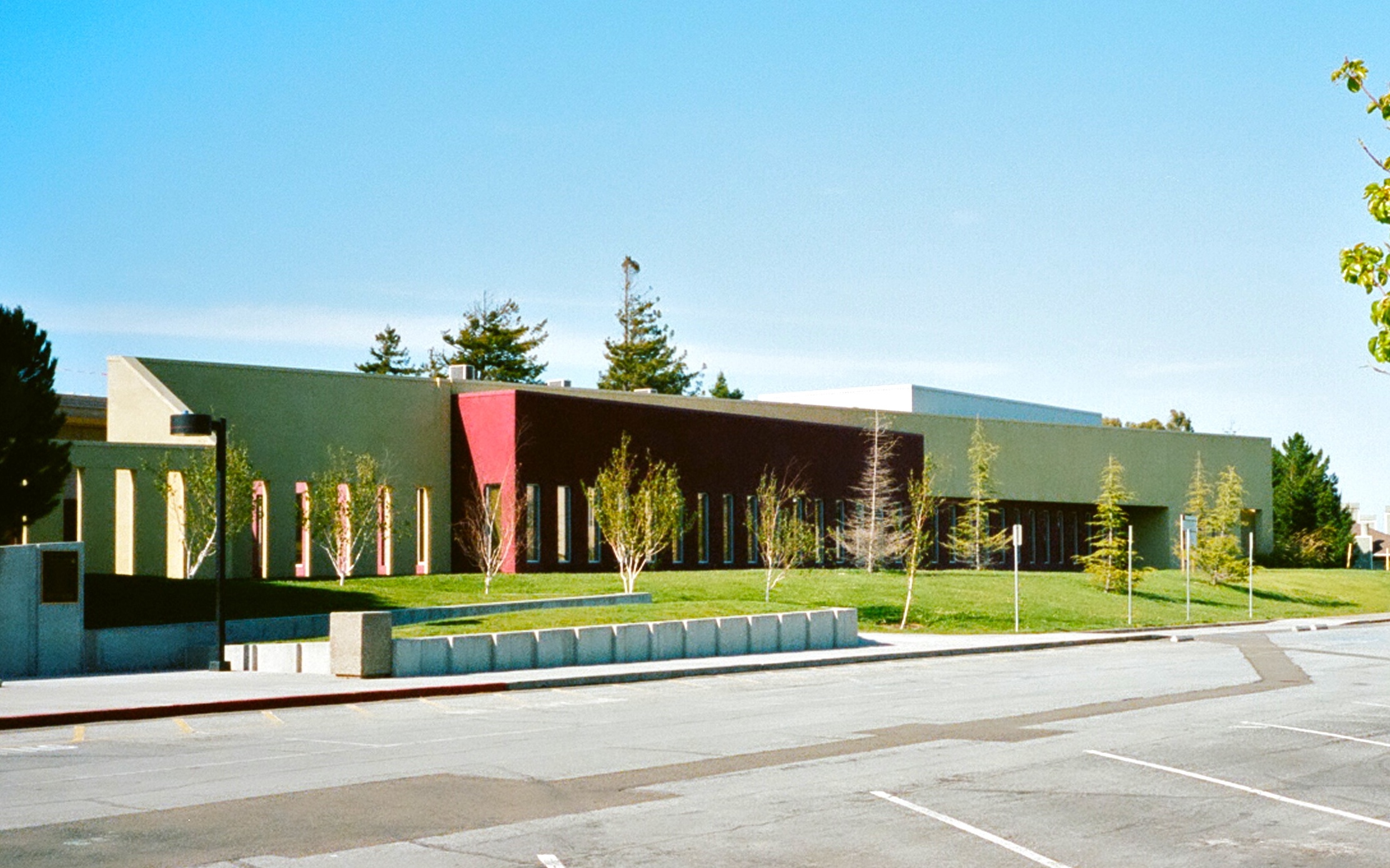 Modern low-rise school building with green and red exterior panels and a parking lot.
