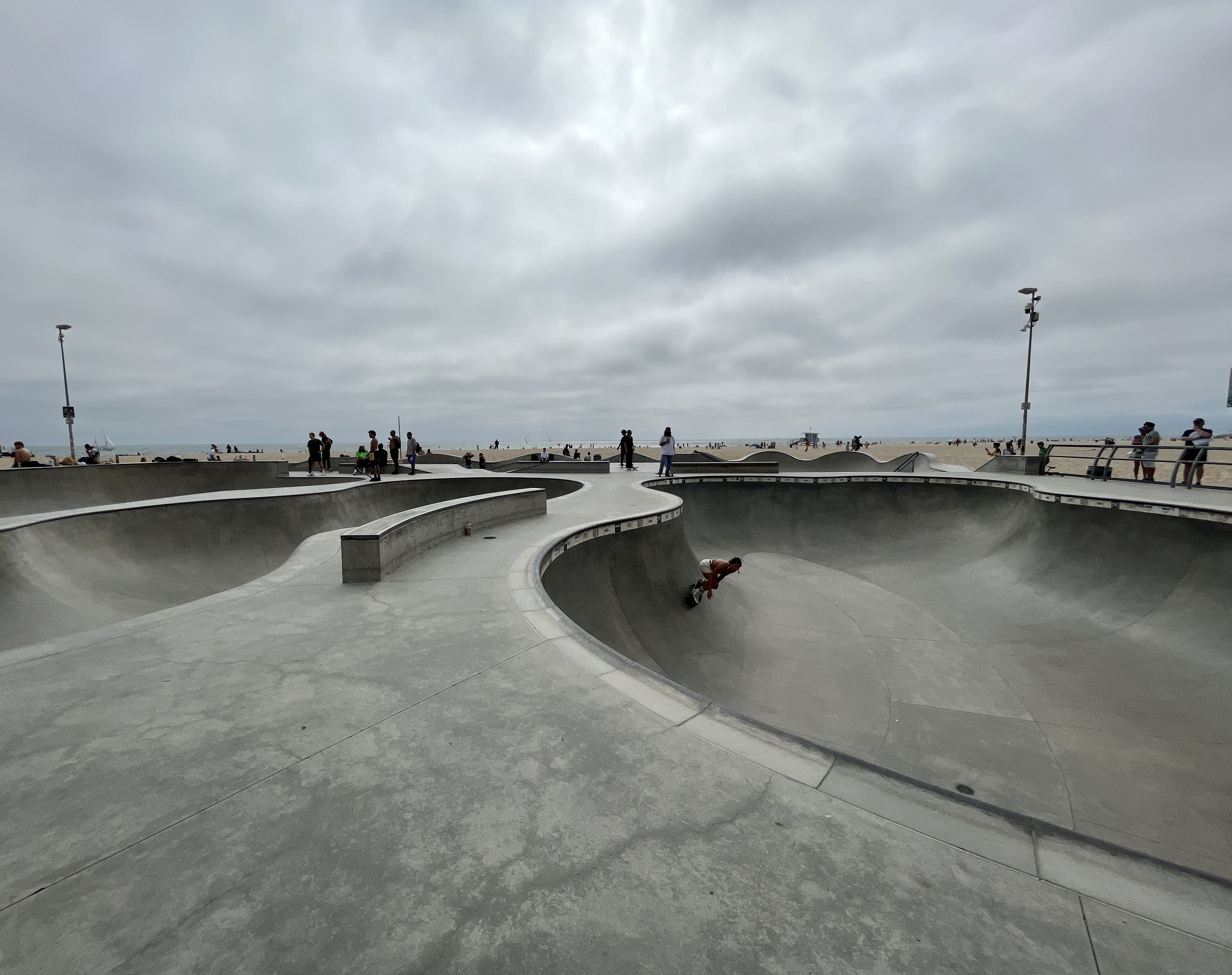 Skater mid-trick inside a concrete bowl at a coastal skate park.
