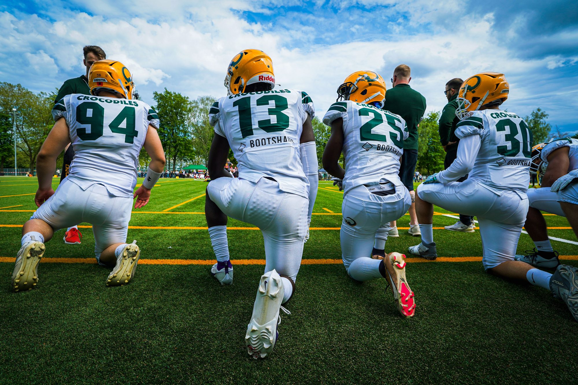 A group of American football players wearing helmets and sports gear kneeling on a green field.