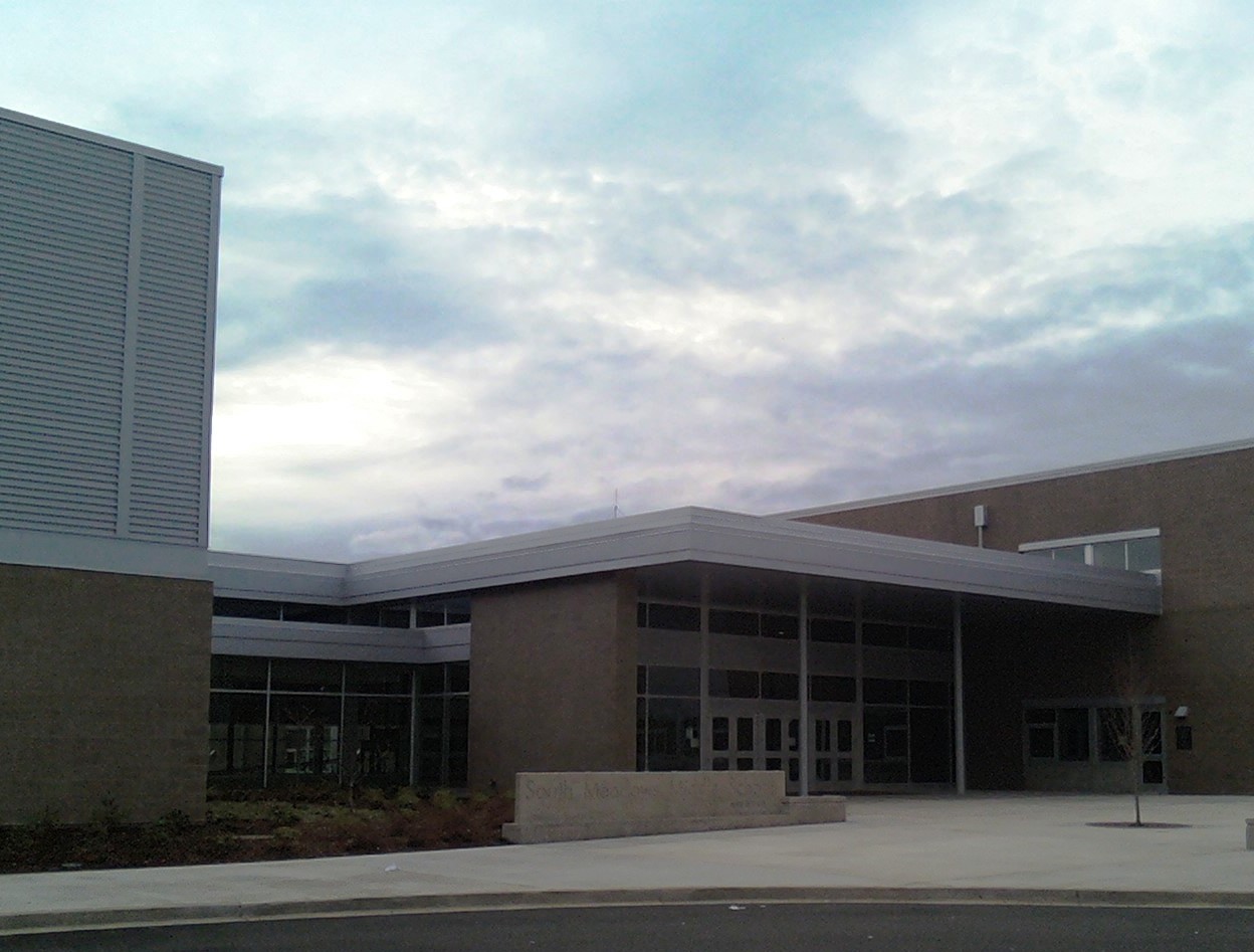 Main entrance of a modern school building with a covered canopy under a cloudy sky.