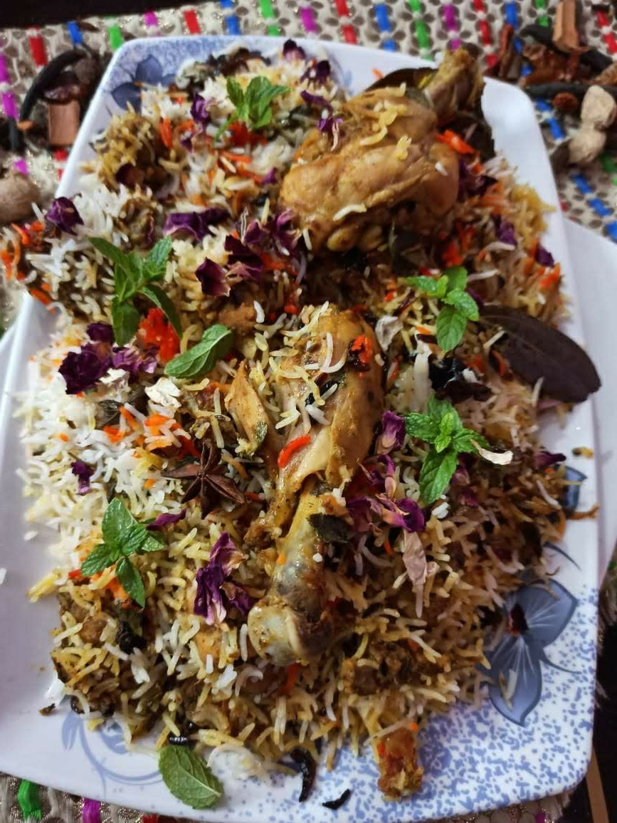 A platter of spiced biryani rice garnished with rose petals, mint, and whole spices.