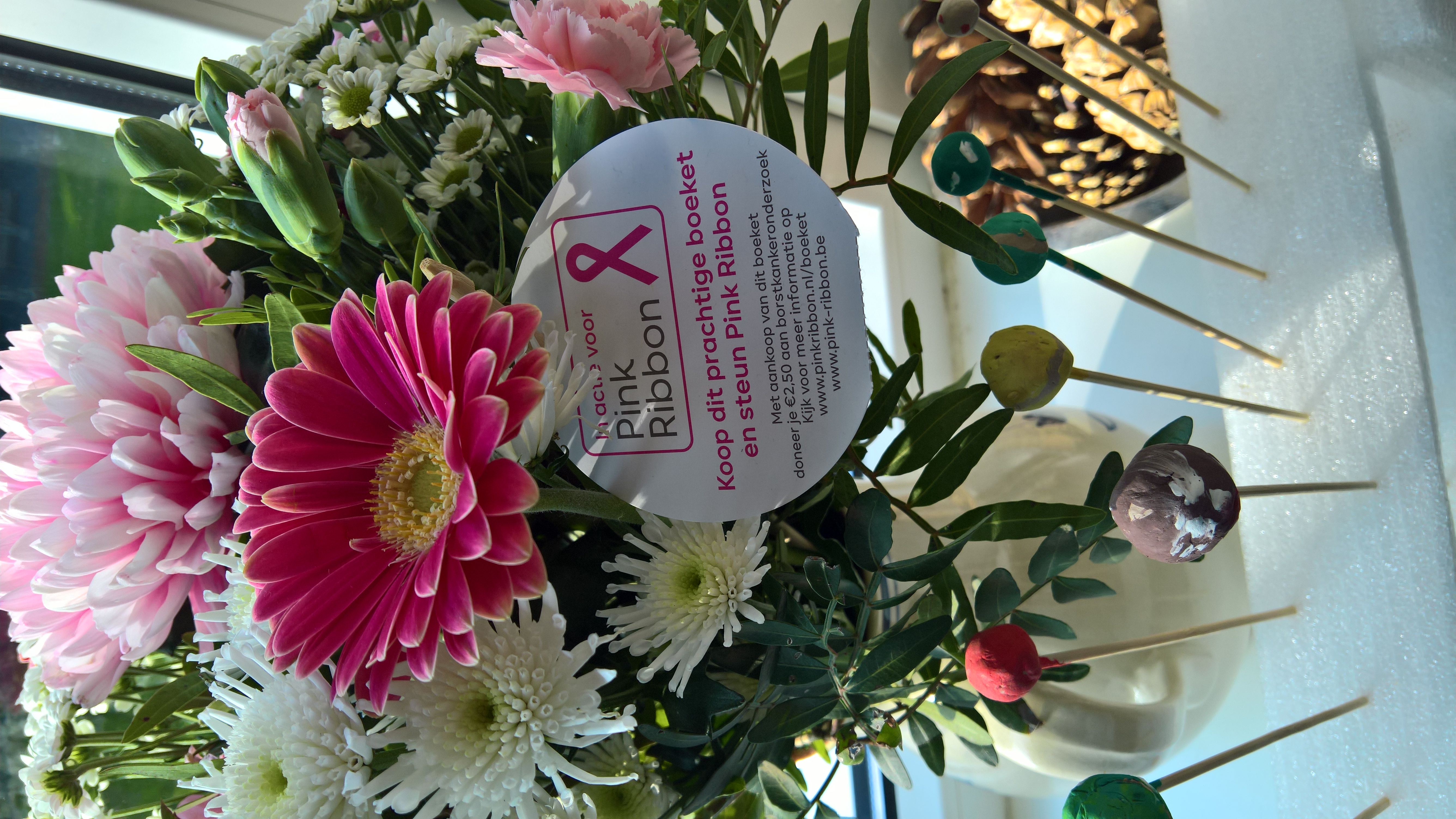 Pink gerbera daisies and white chrysanthemums in a bouquet with a breast cancer awareness card.