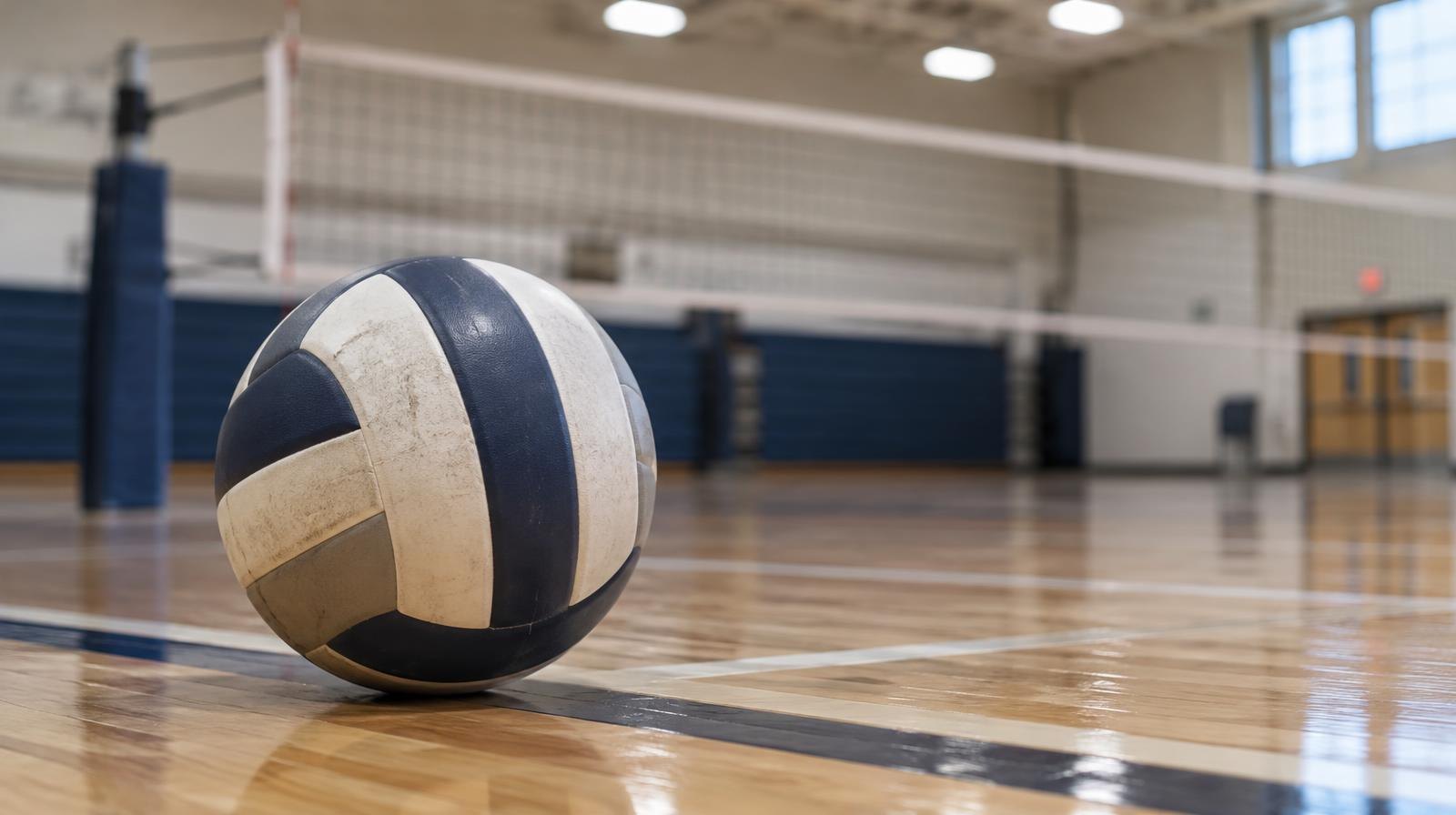 A volleyball resting on a hardwood gymnasium floor near the net.