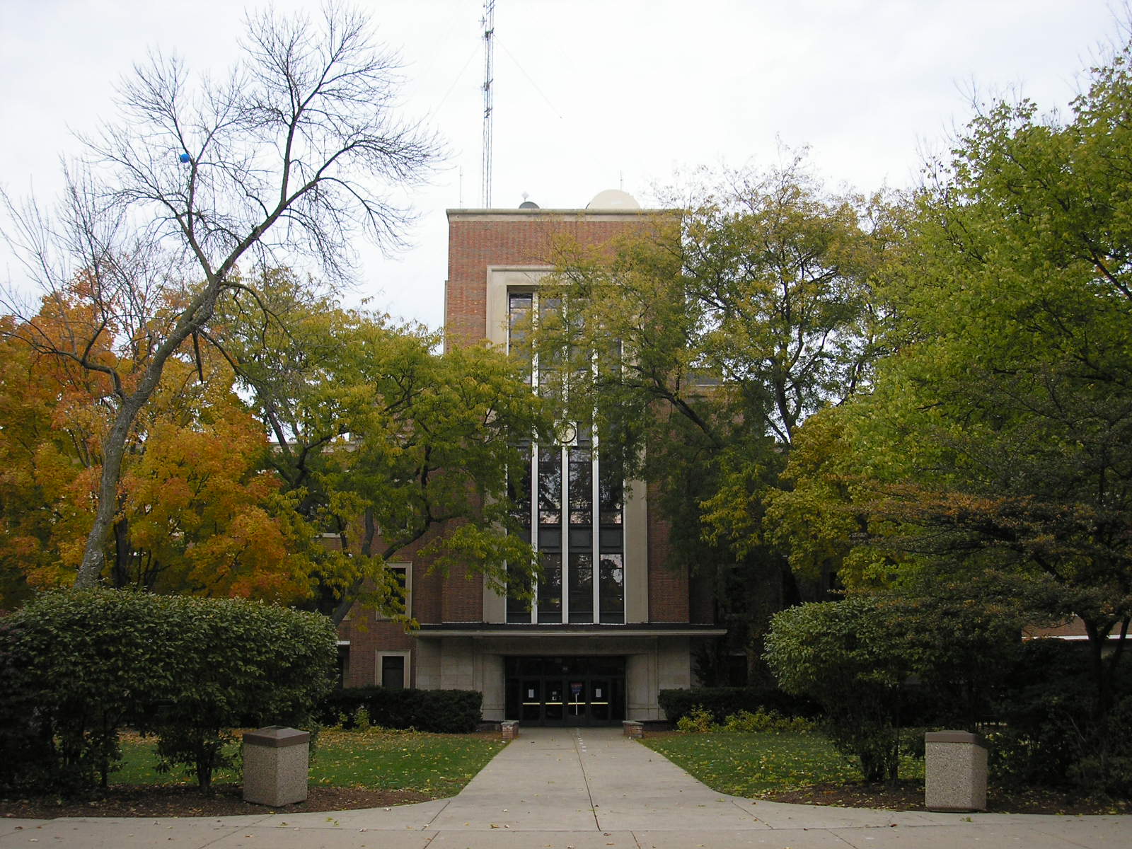 Multi-story brick school building with a central tower, framed by trees with autumn foliage.