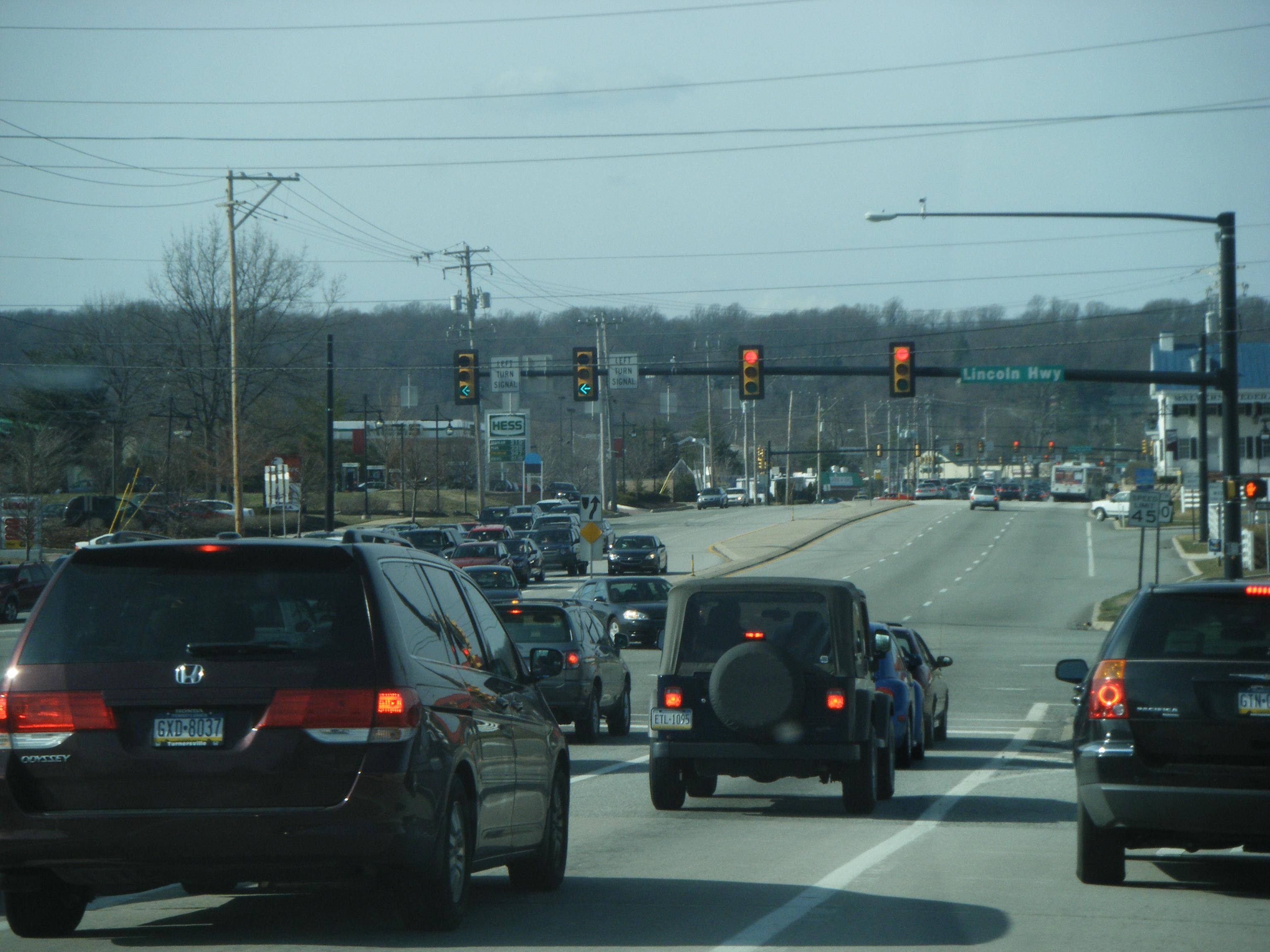 Heavy traffic queued at a multi-lane intersection with red traffic signals overhead.