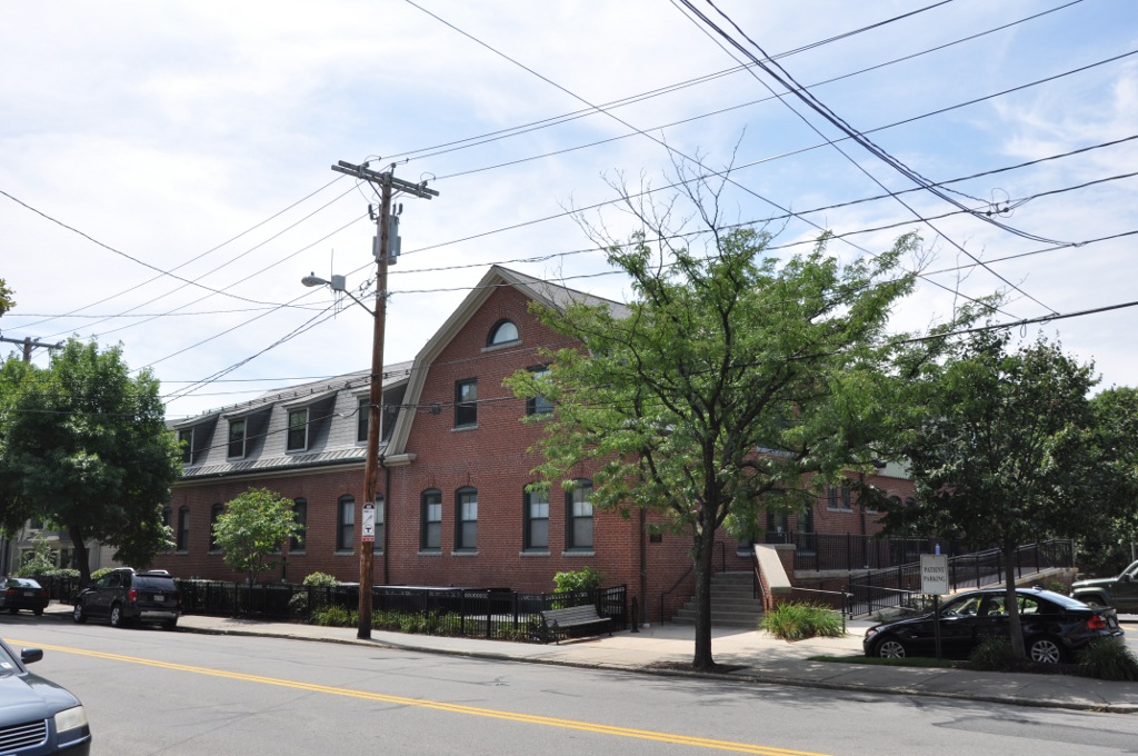 Red brick building with mansard roof on a tree-lined street in Brookline.