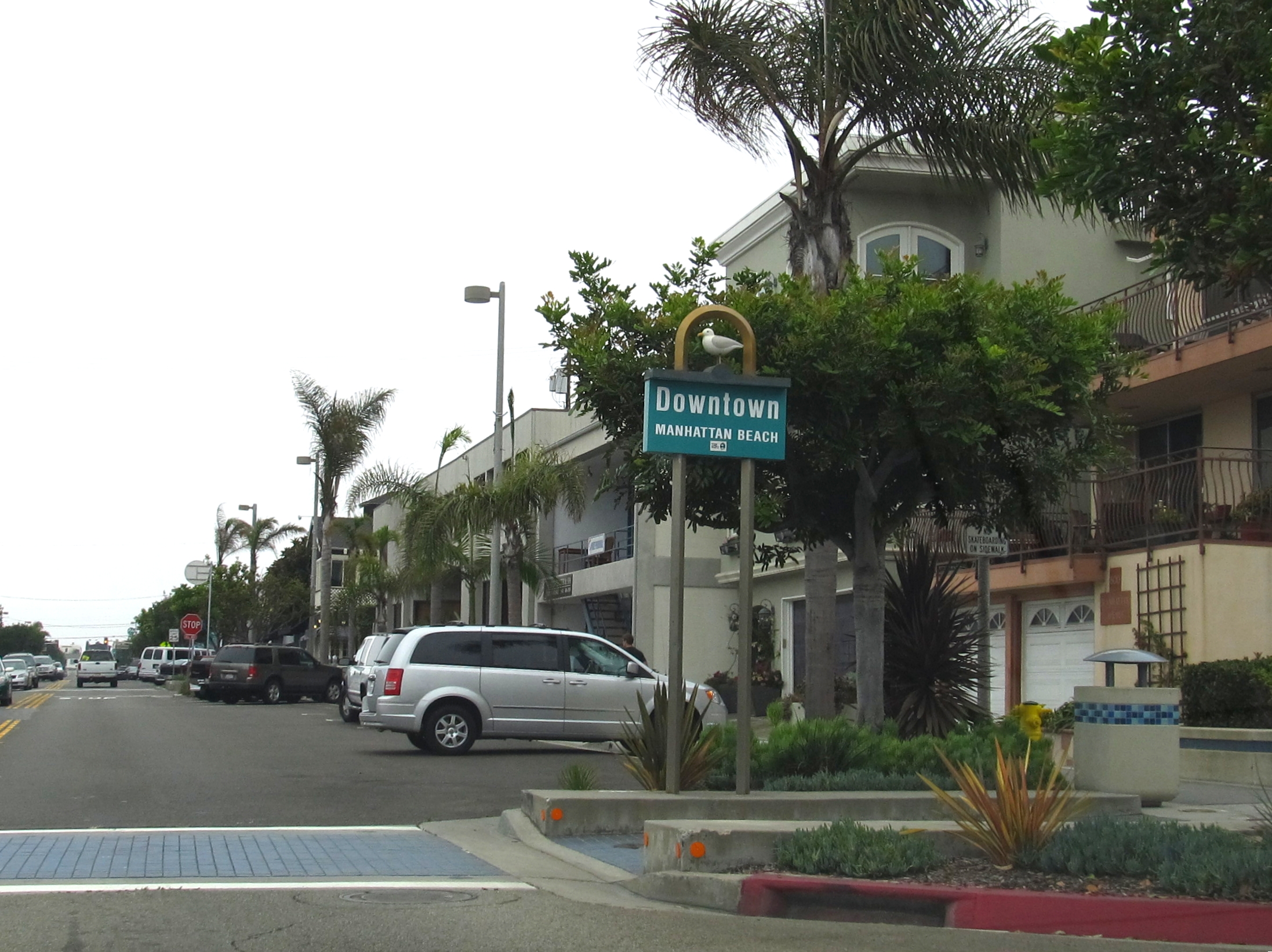 Street scene with a Downtown Manhattan Beach sign, palm trees, and commercial buildings.