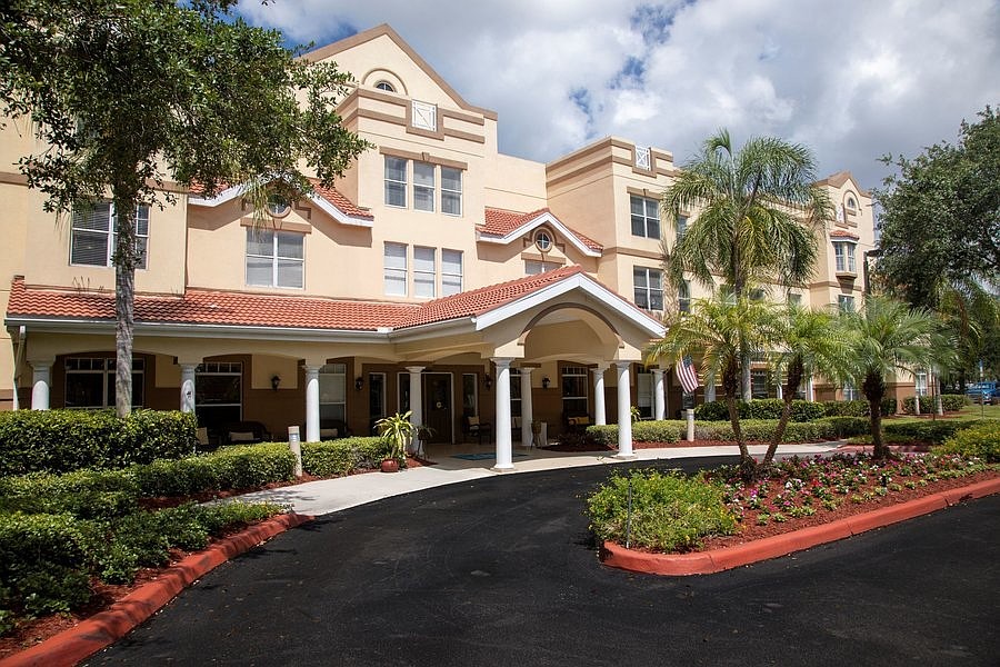 Exterior of the AdviniaCare Naples senior living campus with a covered entrance and landscaped grounds.