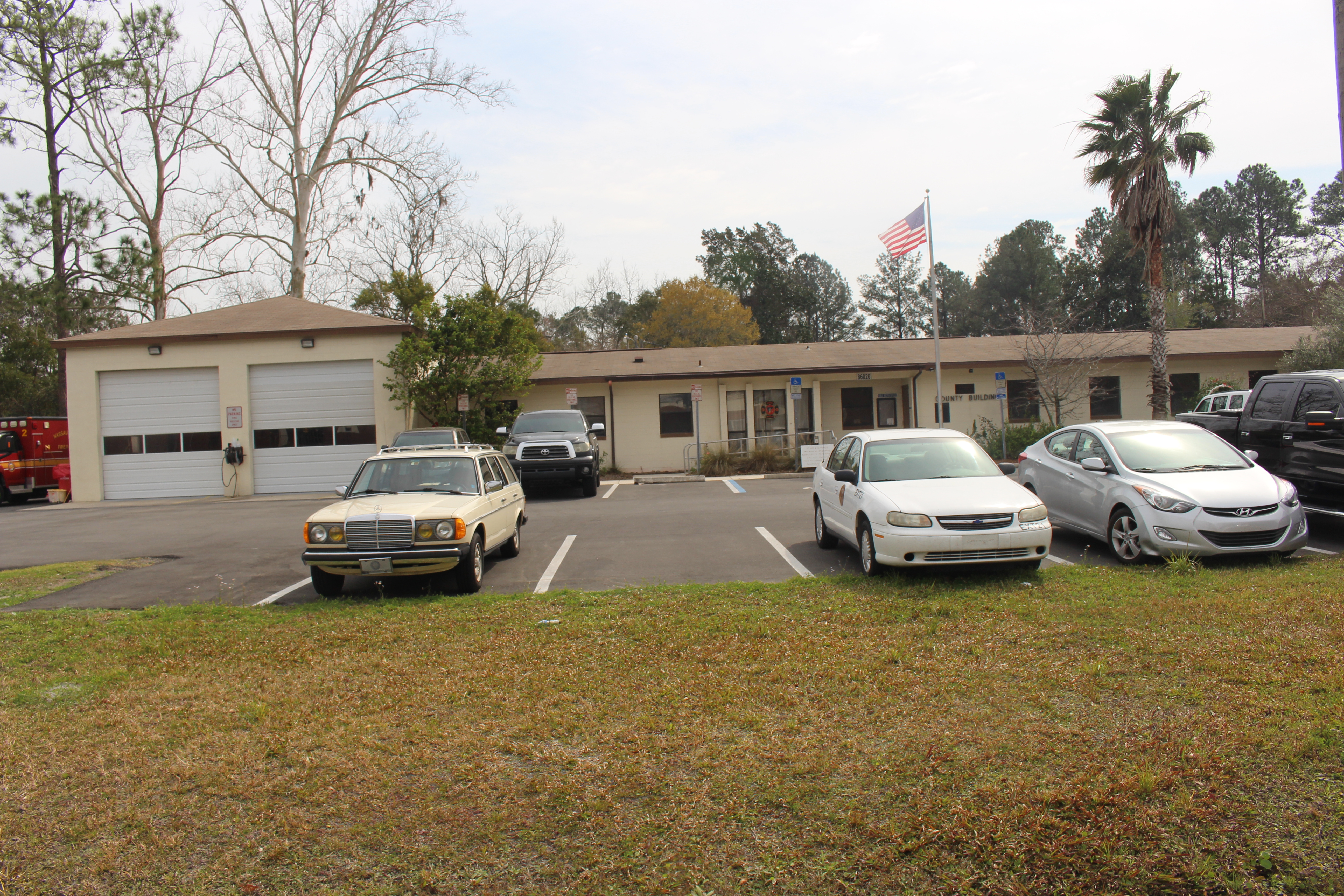 Single-story county government building with garage bays and an American flag out front.