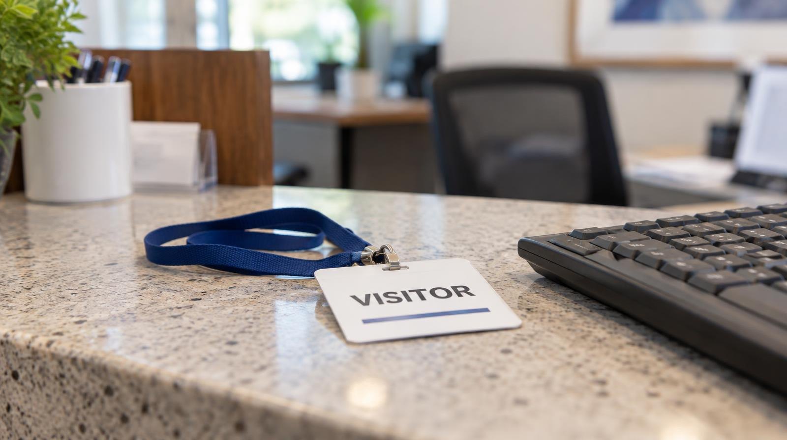 A printed visitor badge with a lanyard on a reception counter beside a keyboard.